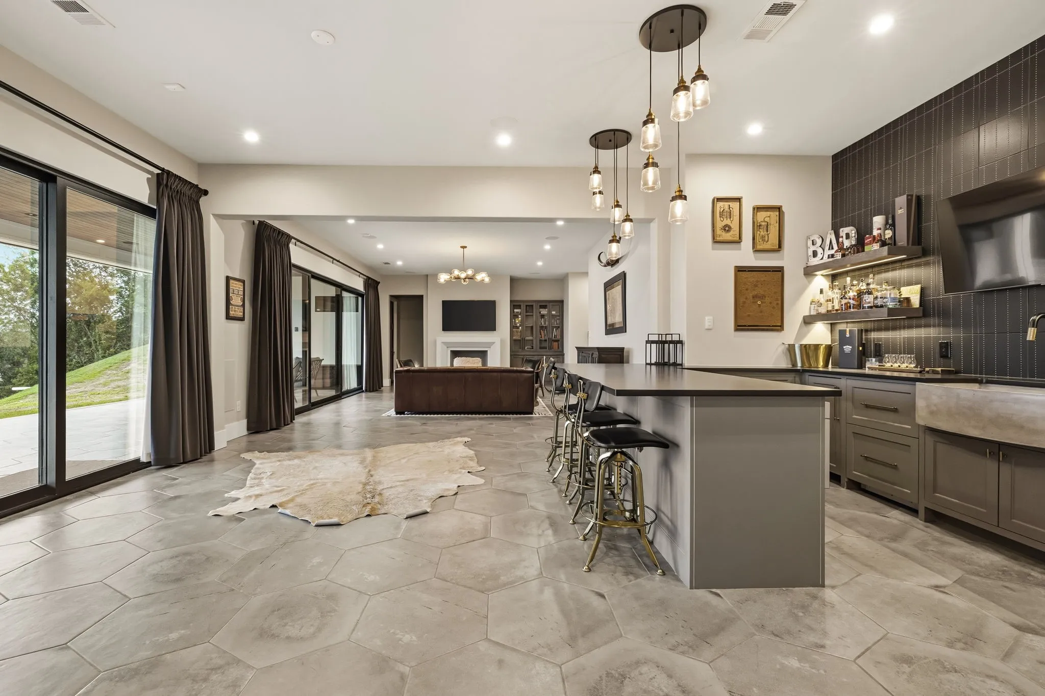 Expansive hexagonal tile flooring extending throughout, full wet bar with dark cabinetry and concrete sink, multiple sliding glass doors, recessed lighting, and modern pendant light fixtures