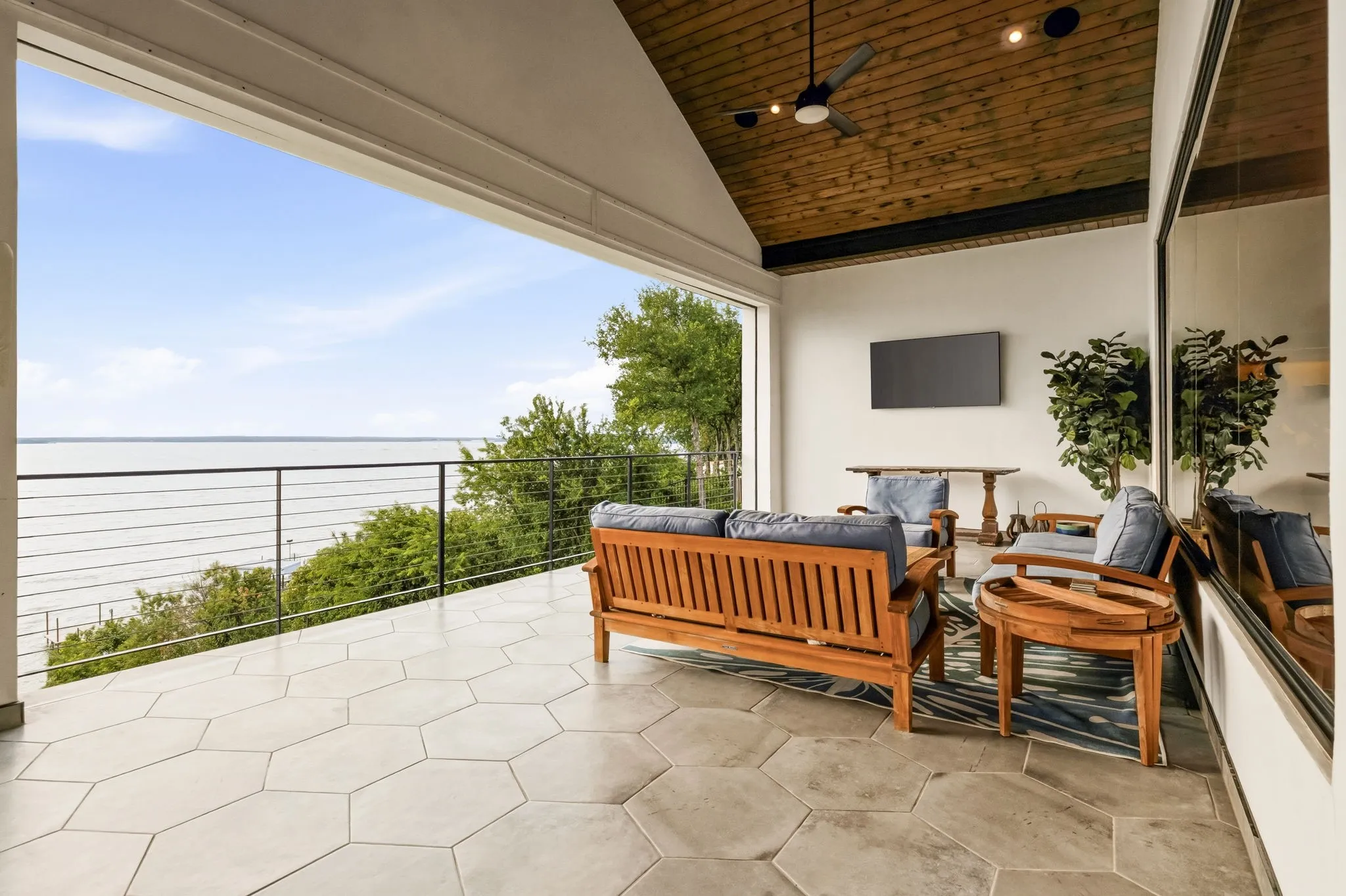 Spacious covered patio featuring hexagonal tile flooring, a wood-paneled vaulted ceiling with a ceiling fan, and a black metal cable railing
