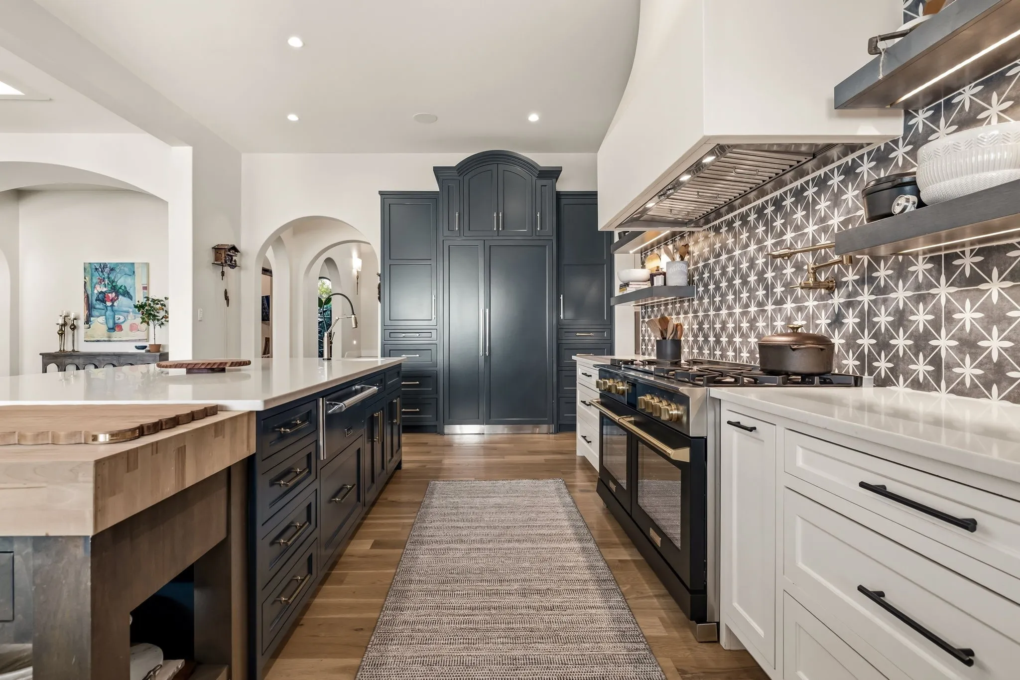 Large kitchen island with wood-finish countertop, custom cabinetry, integrated range with custom hood, and patterned tile backsplash