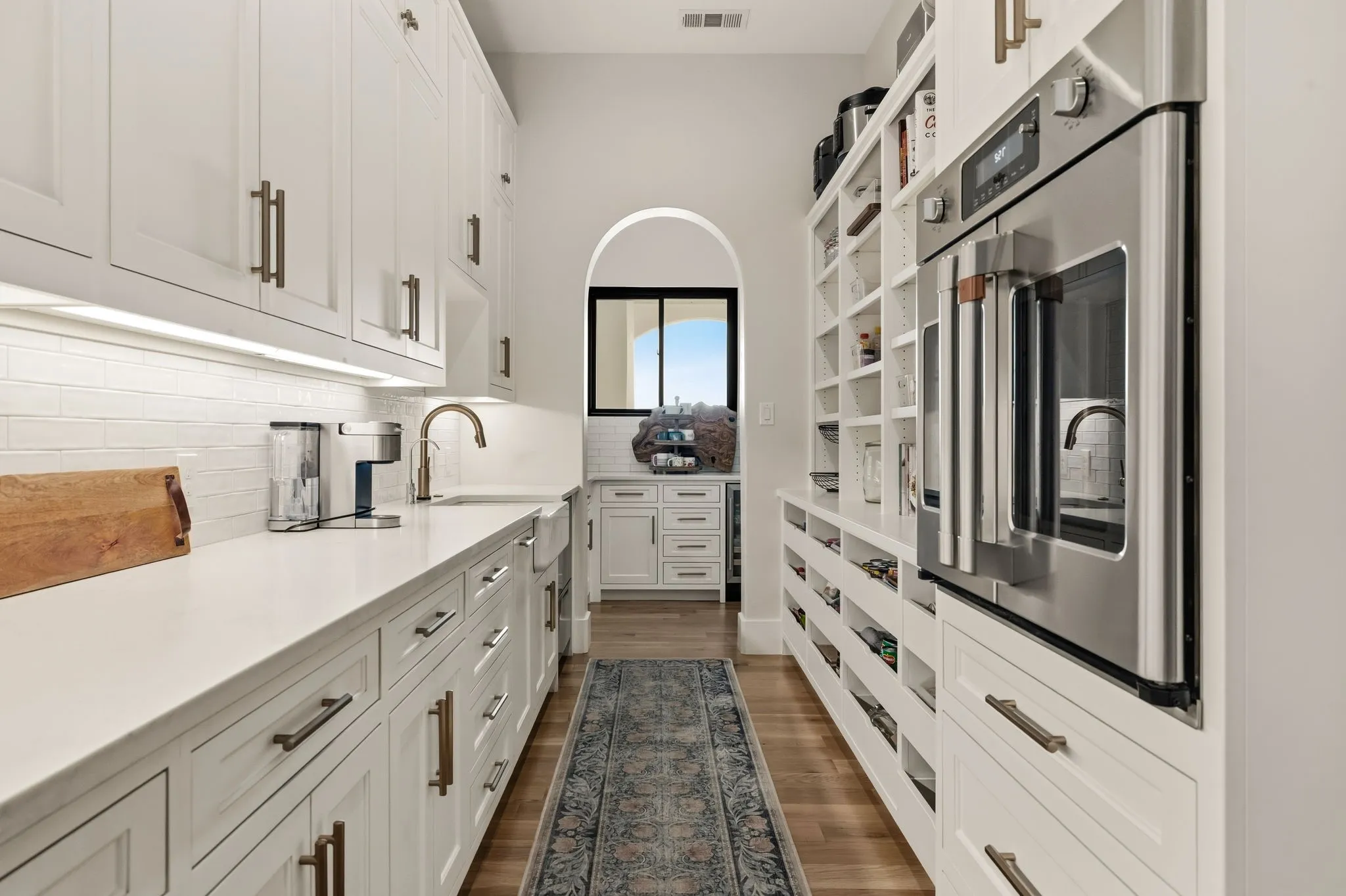 Galley-style kitchen featuring extensive white cabinetry, light-toned countertops, a stainless steel wall oven, and wood-finish flooring