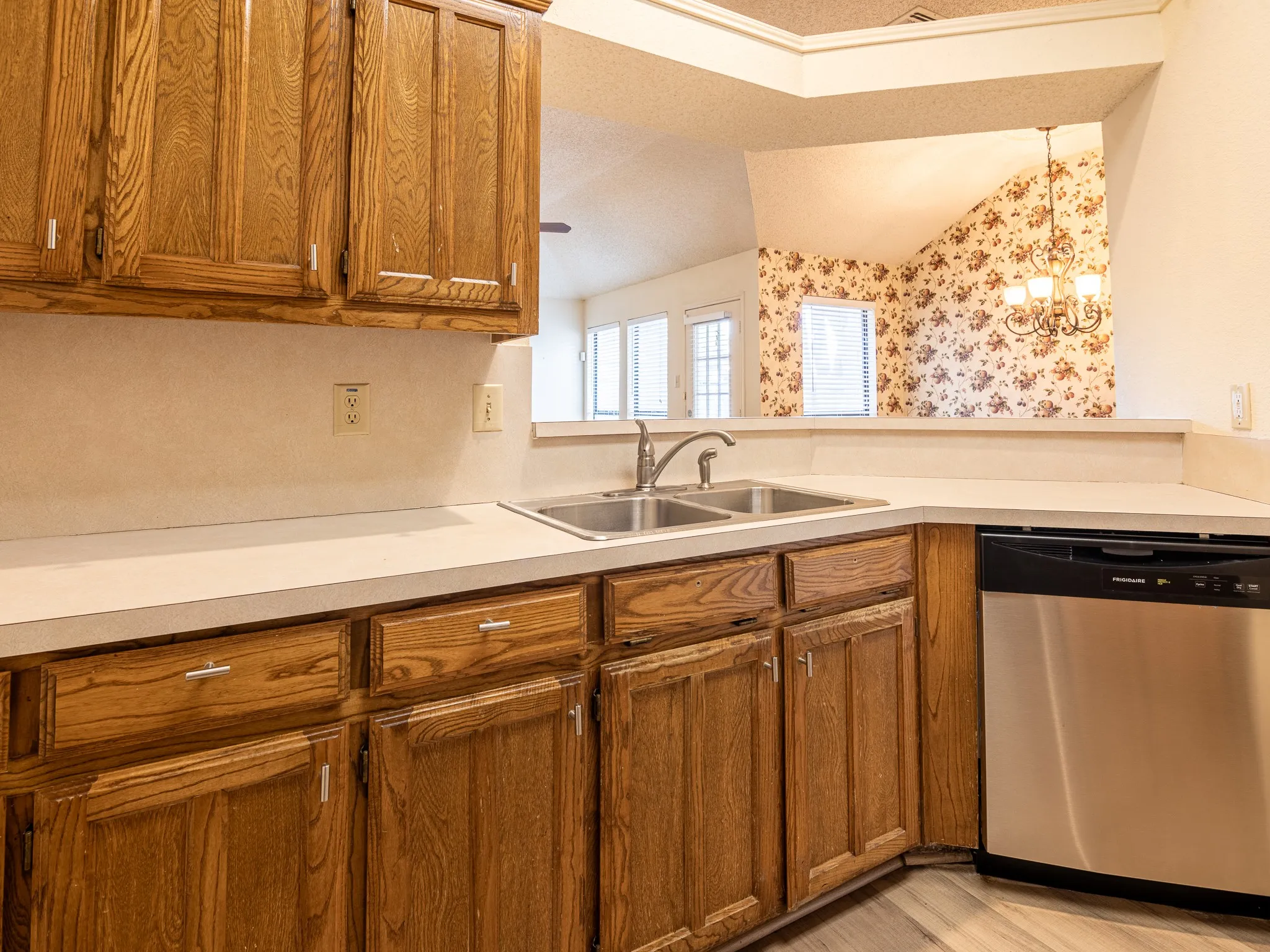 Wood cabinetry, stainless steel sink, chrome faucet, integrated dishwasher, and light countertops