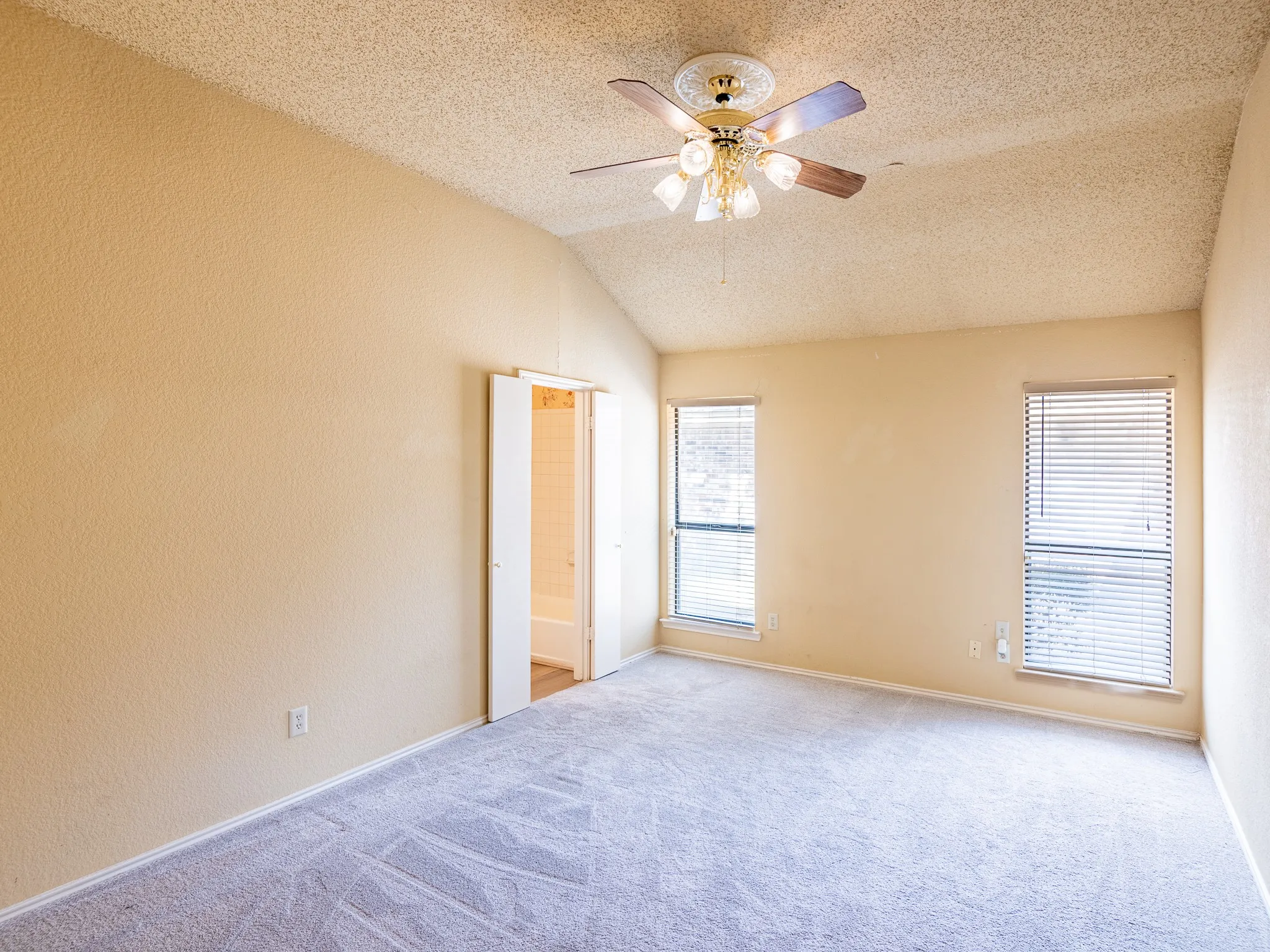 Vaulted ceiling, ceiling fan with integrated lighting, two windows with blinds, light-toned carpeting, and neutral wall tones