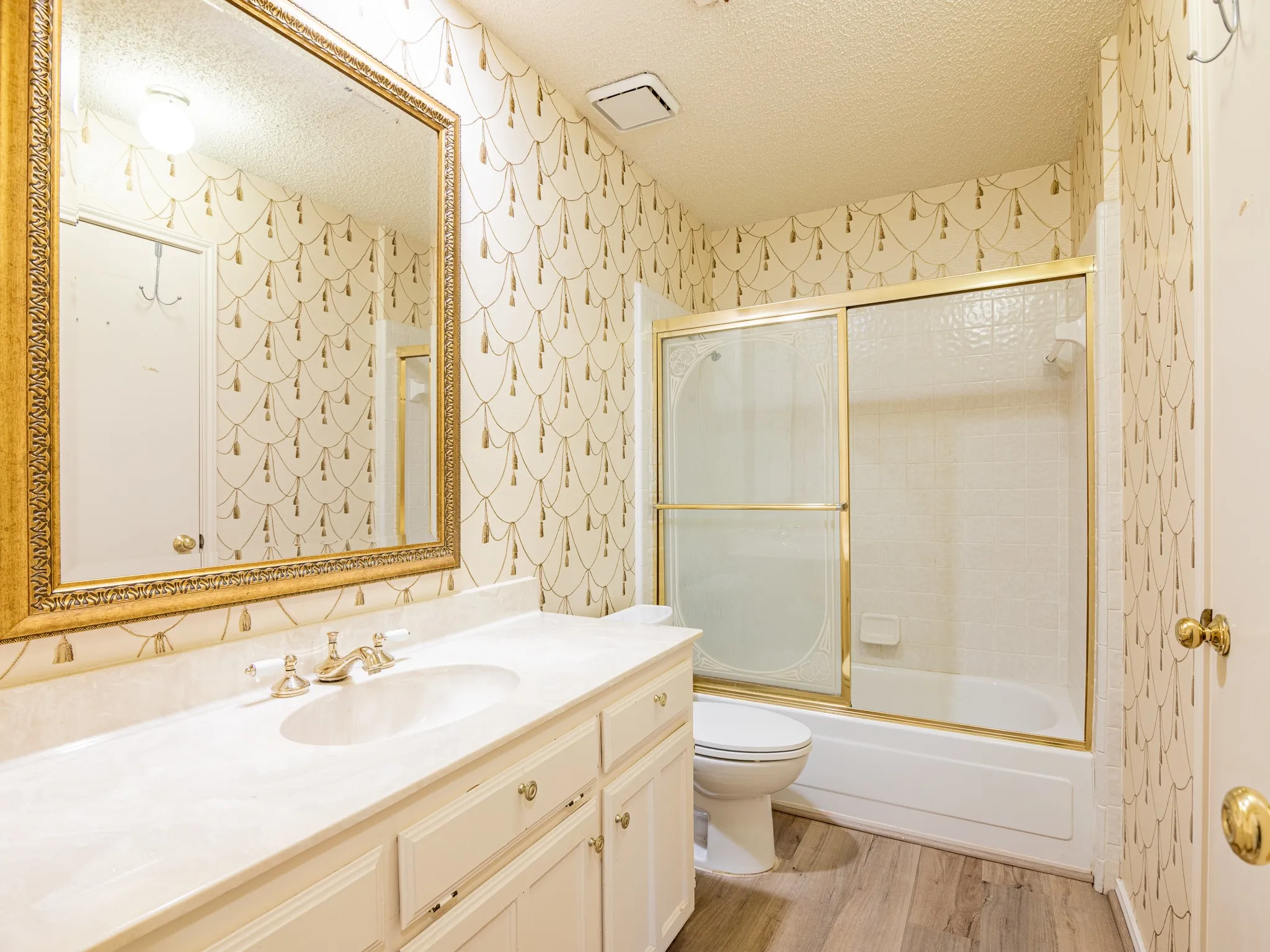 Vanity with integrated sink, gold-tone fixtures, and patterned wallpaper