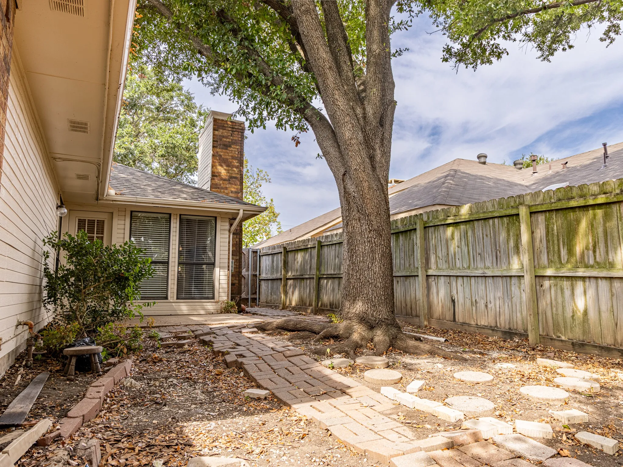Brick patio area with a mature tree and wood fencing
