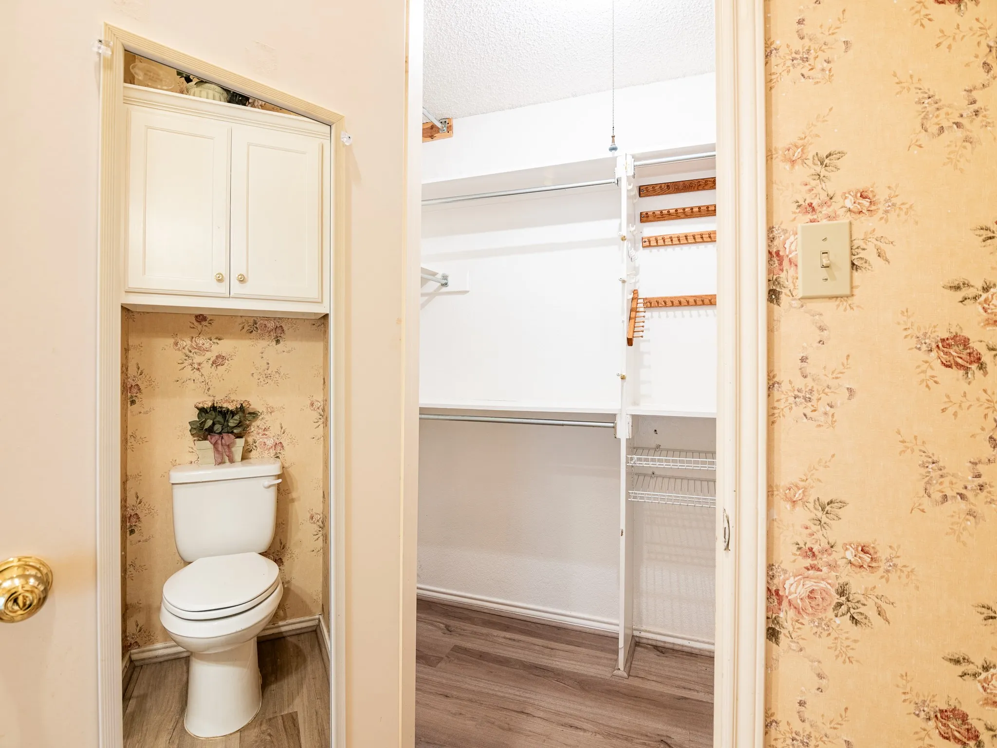 Built-in storage cabinetry above commode, wood-finish flooring, and organized closet shelving