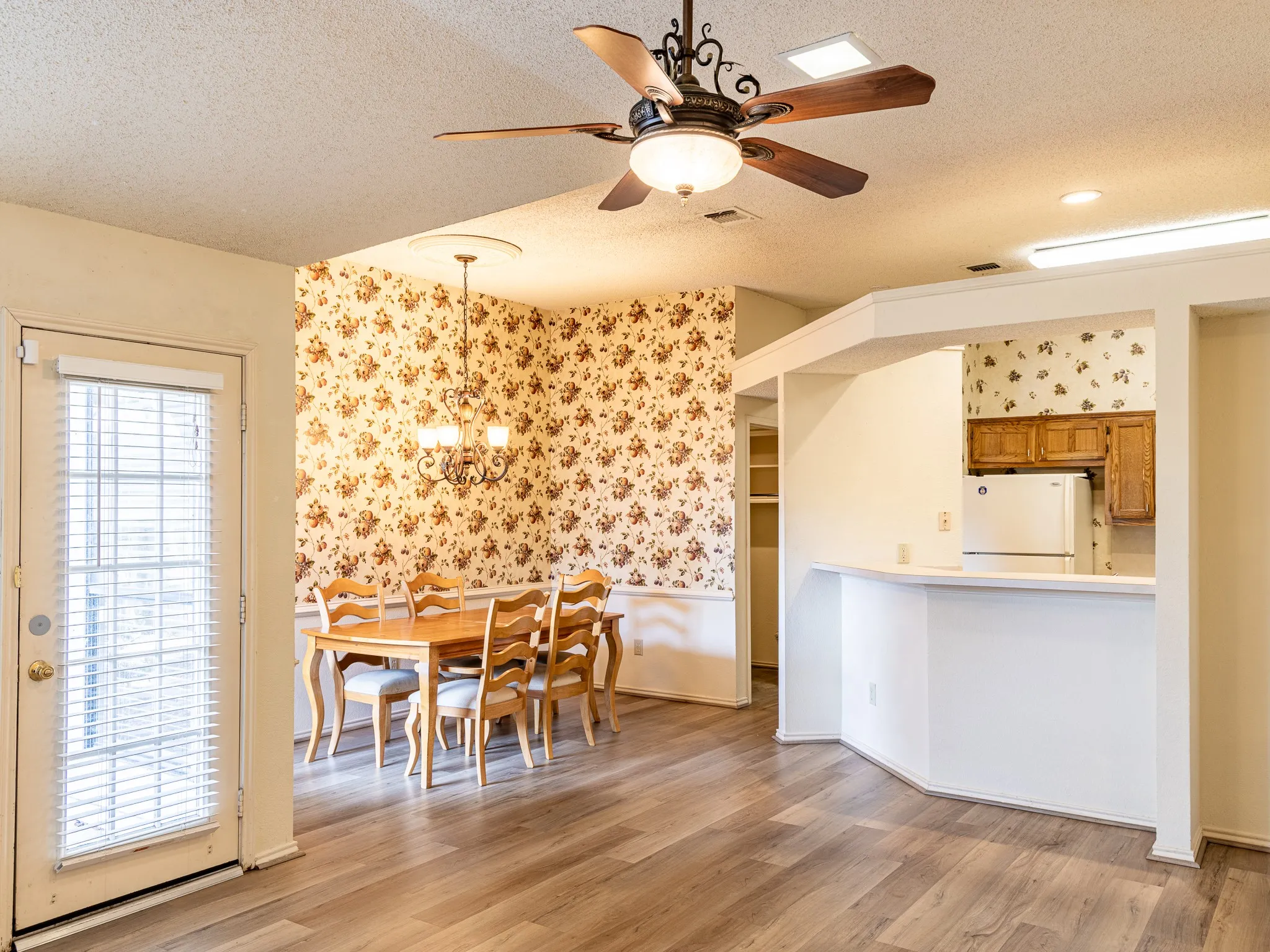 Wood-finish flooring throughout, ceiling fan with integrated lighting, kitchen pass-through with breakfast bar, built-in shelving, and a glass-paneled door