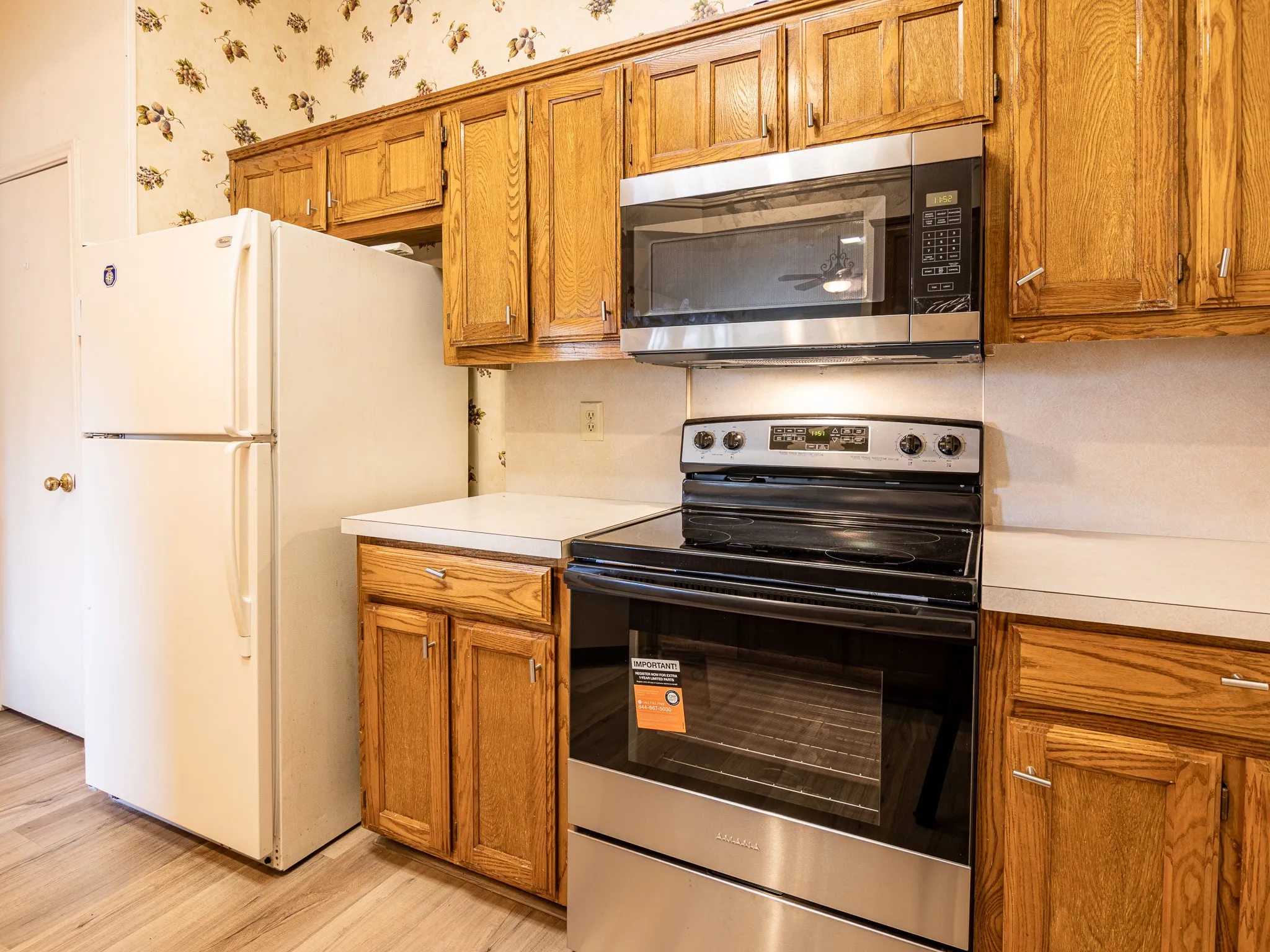 Wood-finish flooring, wood cabinetry, white countertops, stainless steel microwave, and a black electric range