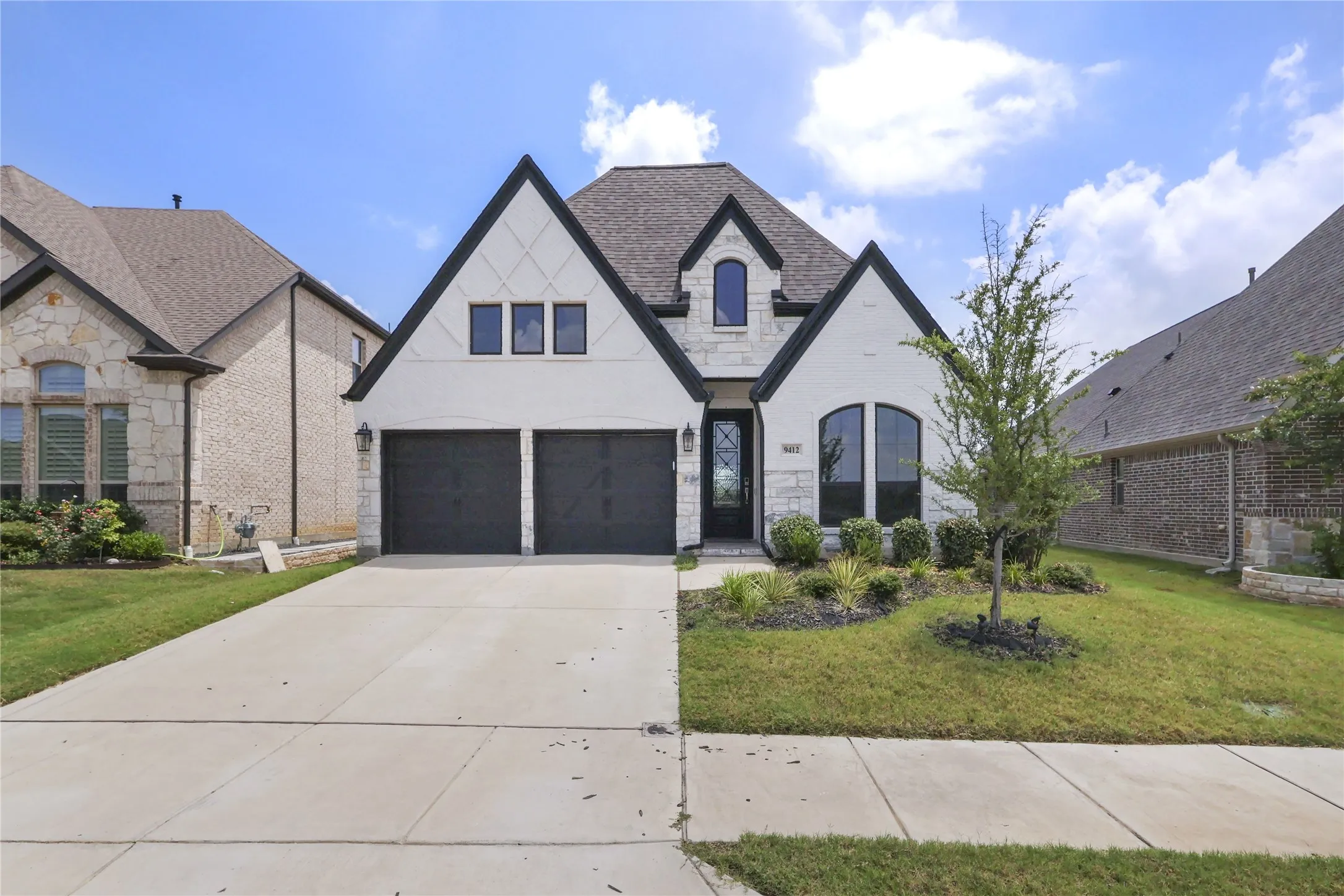 Modern facade with black trim detailing, two-car garage, arched entryways, and a landscaped front yard