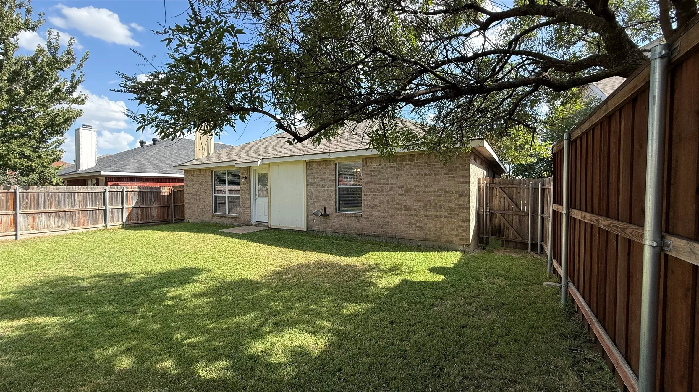 Expansive backyard featuring a manicured lawn, full perimeter privacy fencing, and a brick exterior