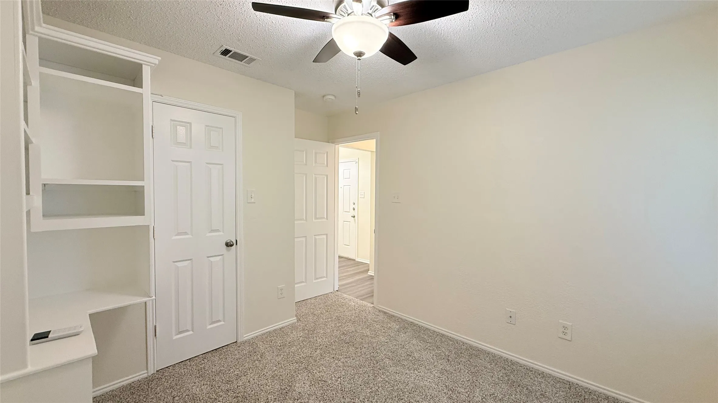 Built-in shelving with desk, overhead lighting with ceiling fan, and grey carpet flooring