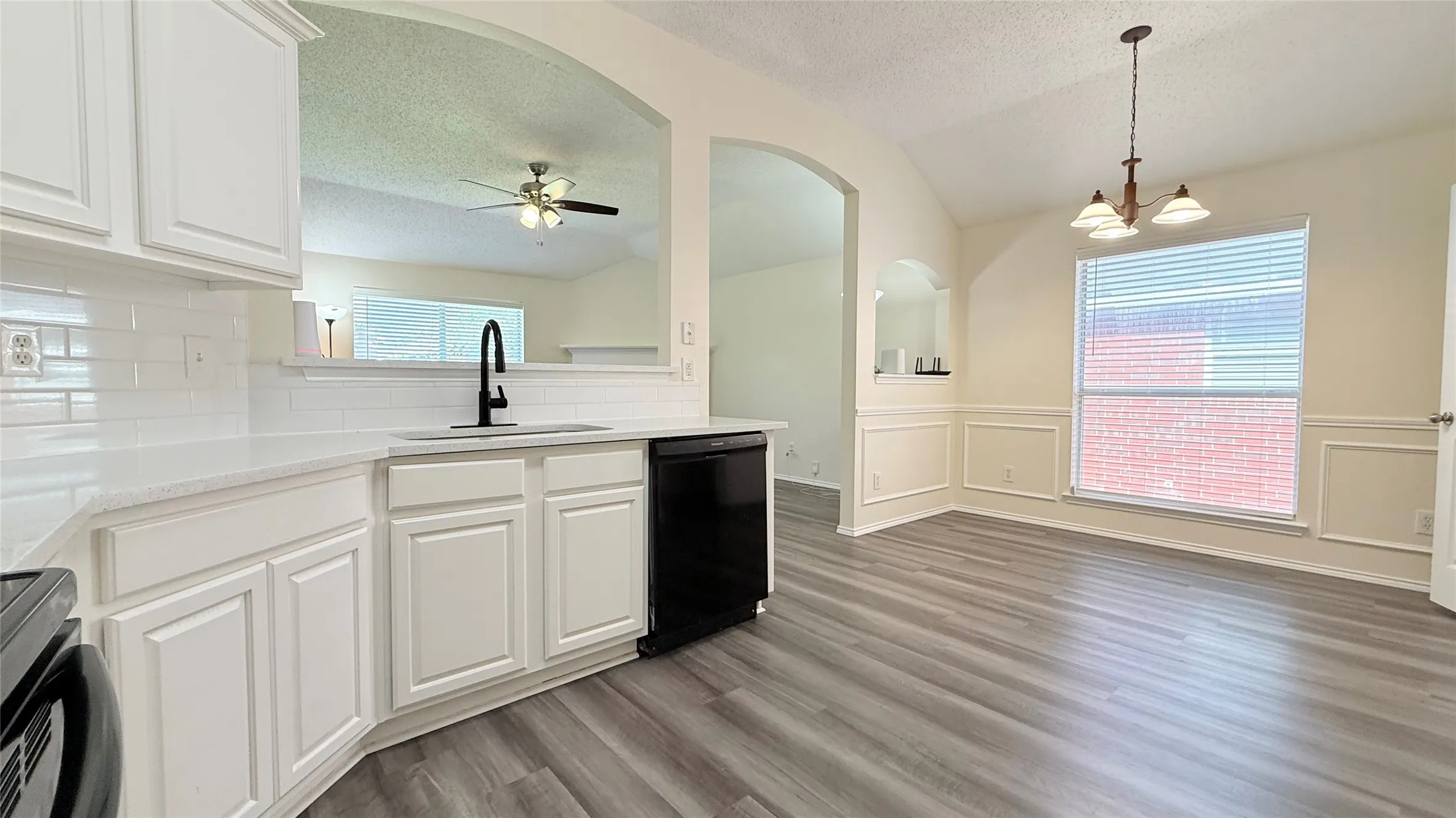 Kitchen featuring white cabinetry, solid surface countertops, a white subway tile backsplash, and a black dishwasher