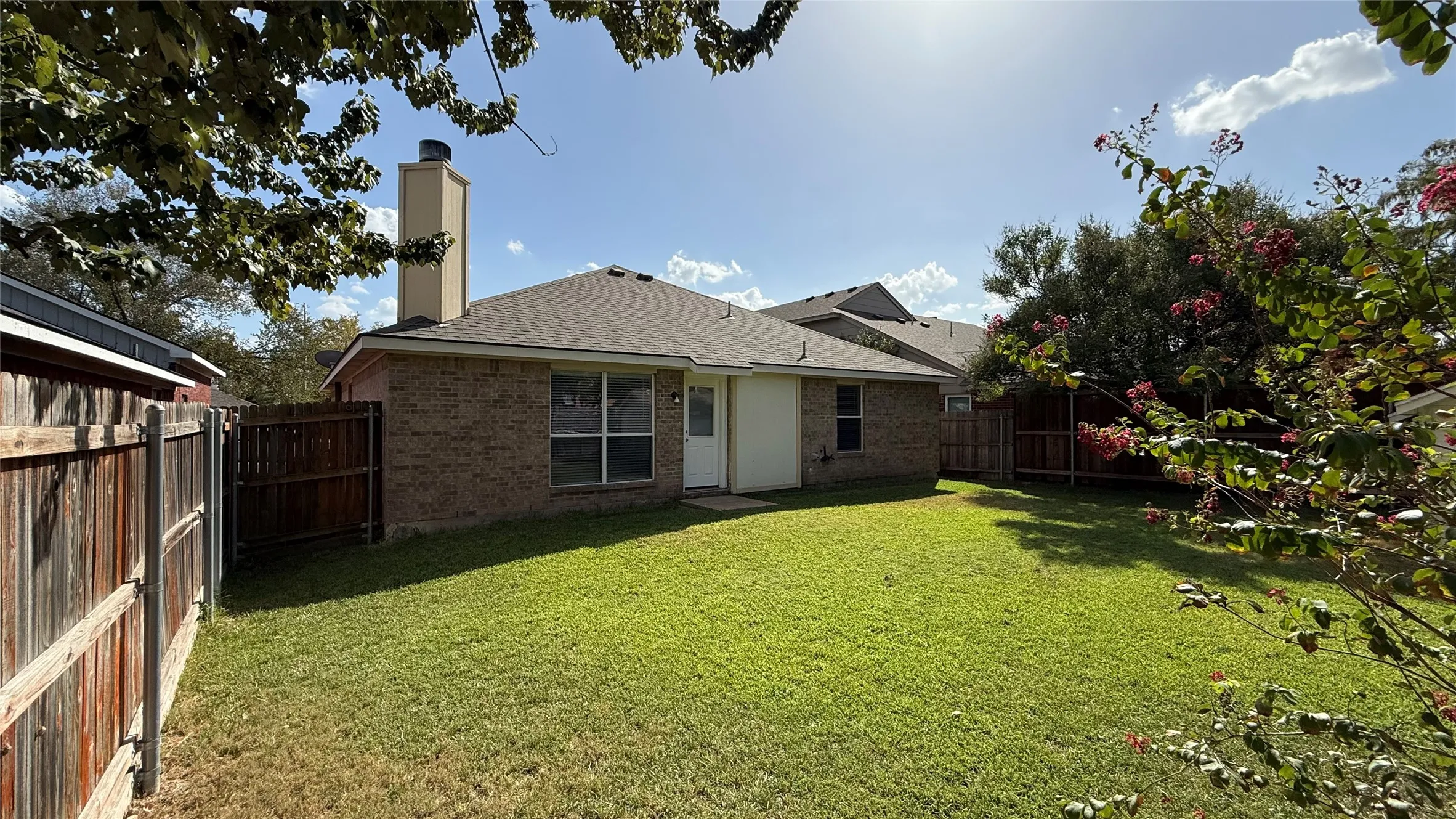 Expansive green lawn with mature perimeter trees, brick exterior, and a built-in chimney feature