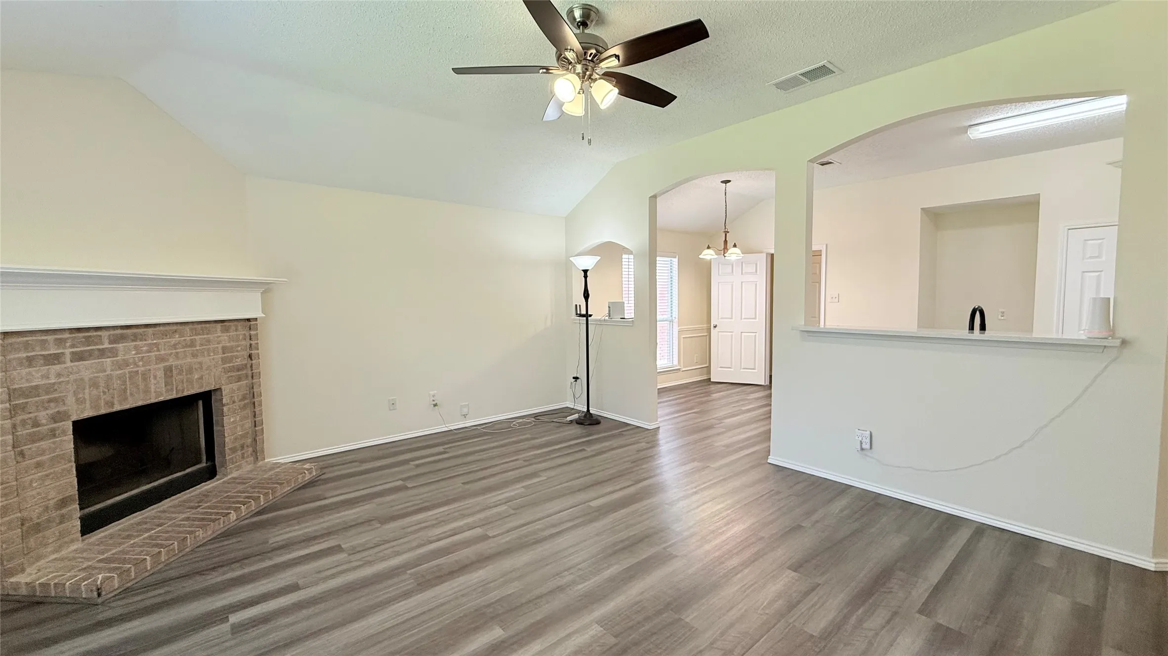Living area featuring a brick fireplace with a white mantel, vaulted ceiling, and wood-finish flooring