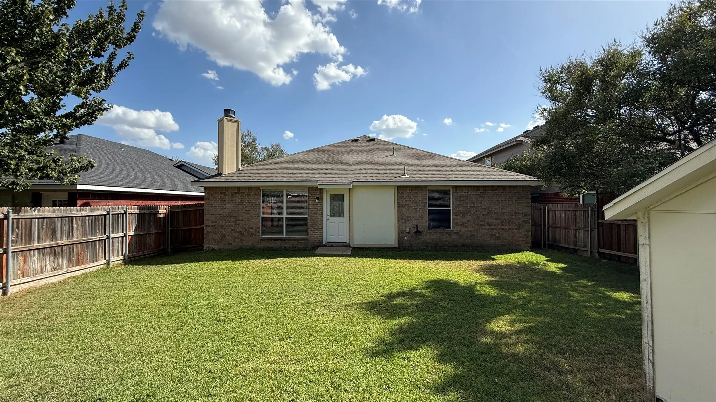 Expansive backyard with a manicured lawn, full privacy fencing, and a brick exterior home with a gabled roofline