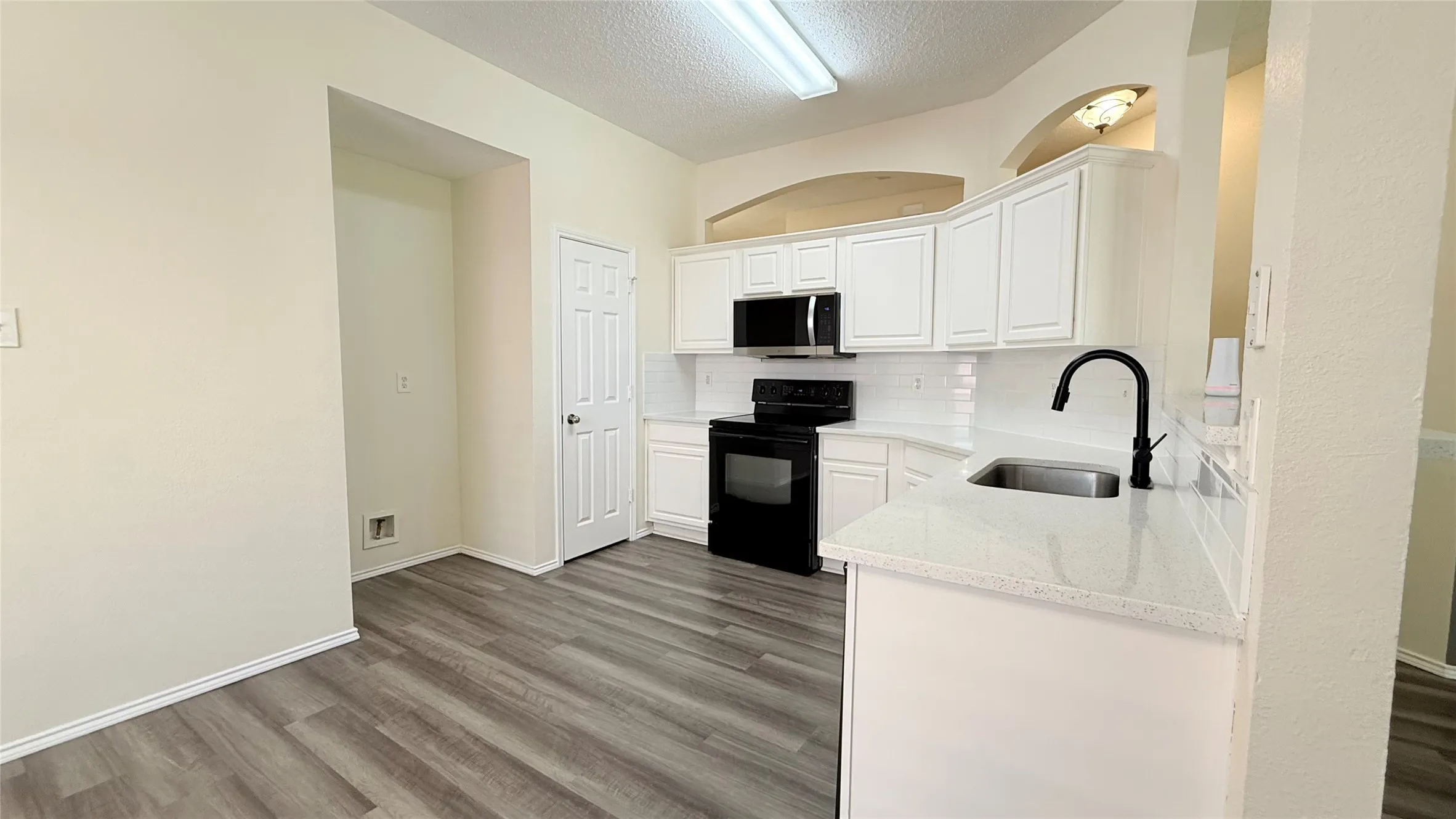 Kitchen featuring white cabinetry, light-toned countertops, a matte black faucet, and wood-finish flooring
