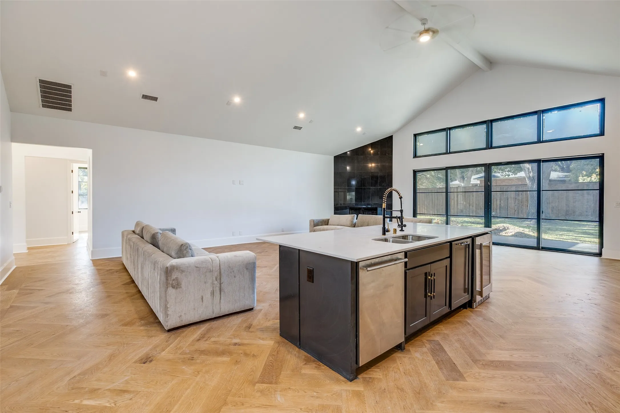 Vaulted ceiling with a ceiling fan, herringbone wood-finish flooring, and an island with an integrated sink and appliances