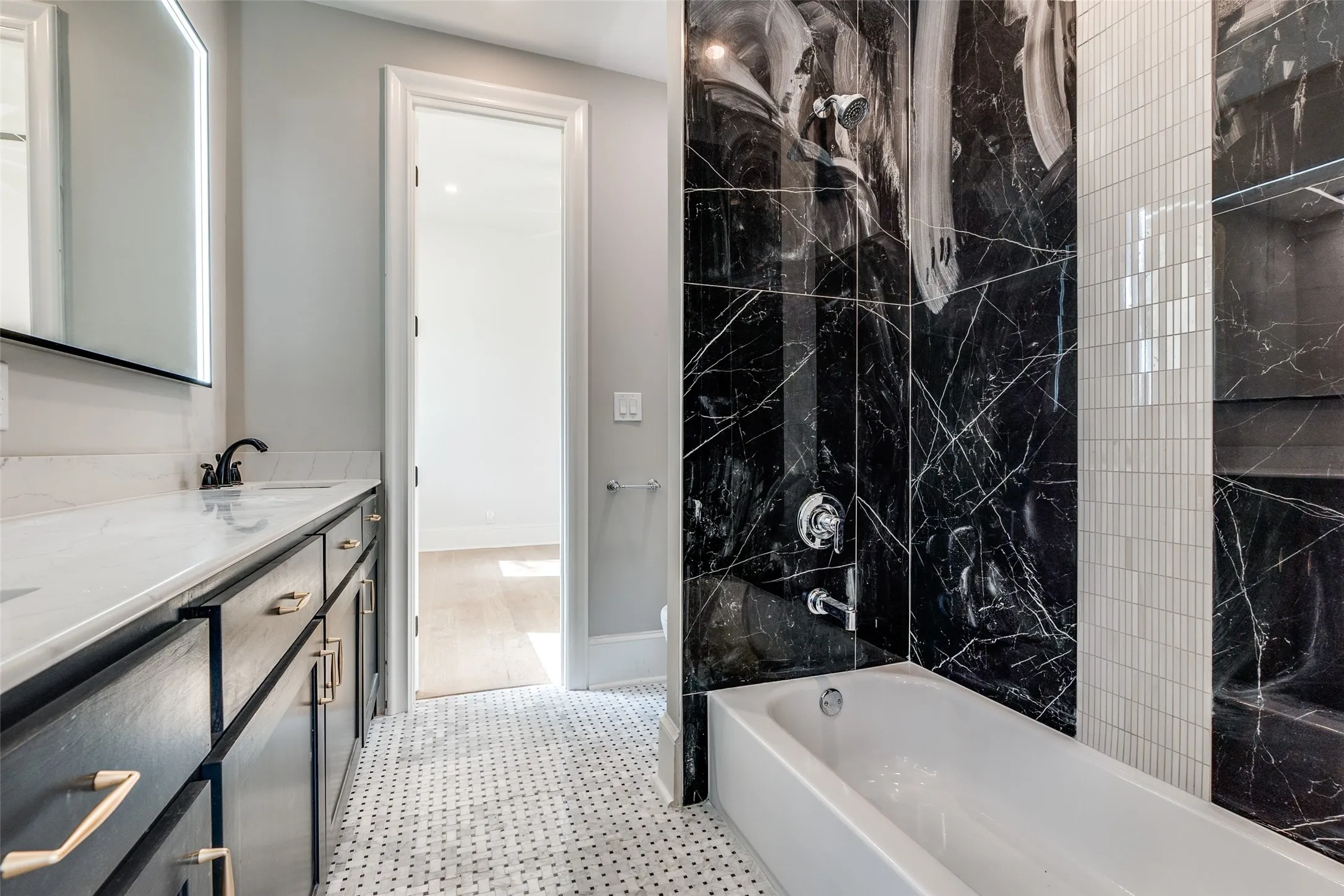 Bathroom featuring a black vanity with a light-colored countertop, dual sinks, and a built-in bathtub with black and white tiled surround