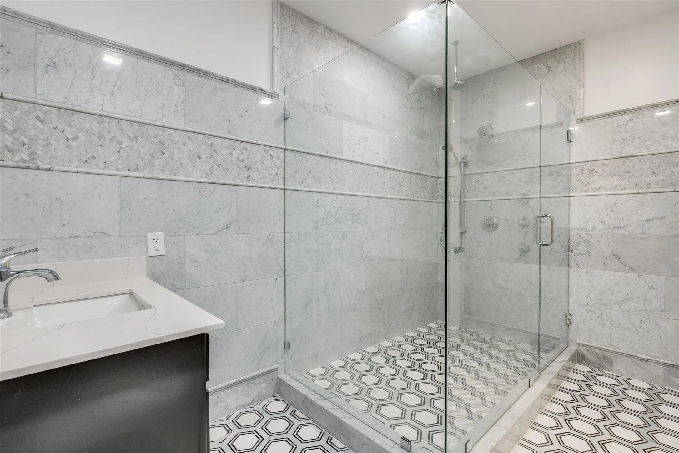 Glass-enclosed shower with a hex tile floor, complemented by a vanity with a white countertop and undermount sink