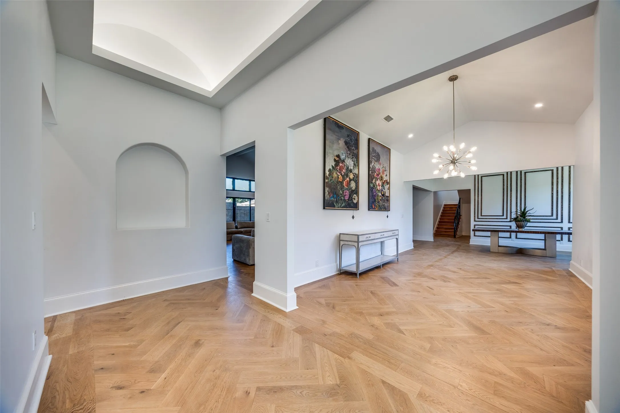 Herringbone wood-finish flooring, vaulted ceilings, recessed lighting, and a modern chandelier
