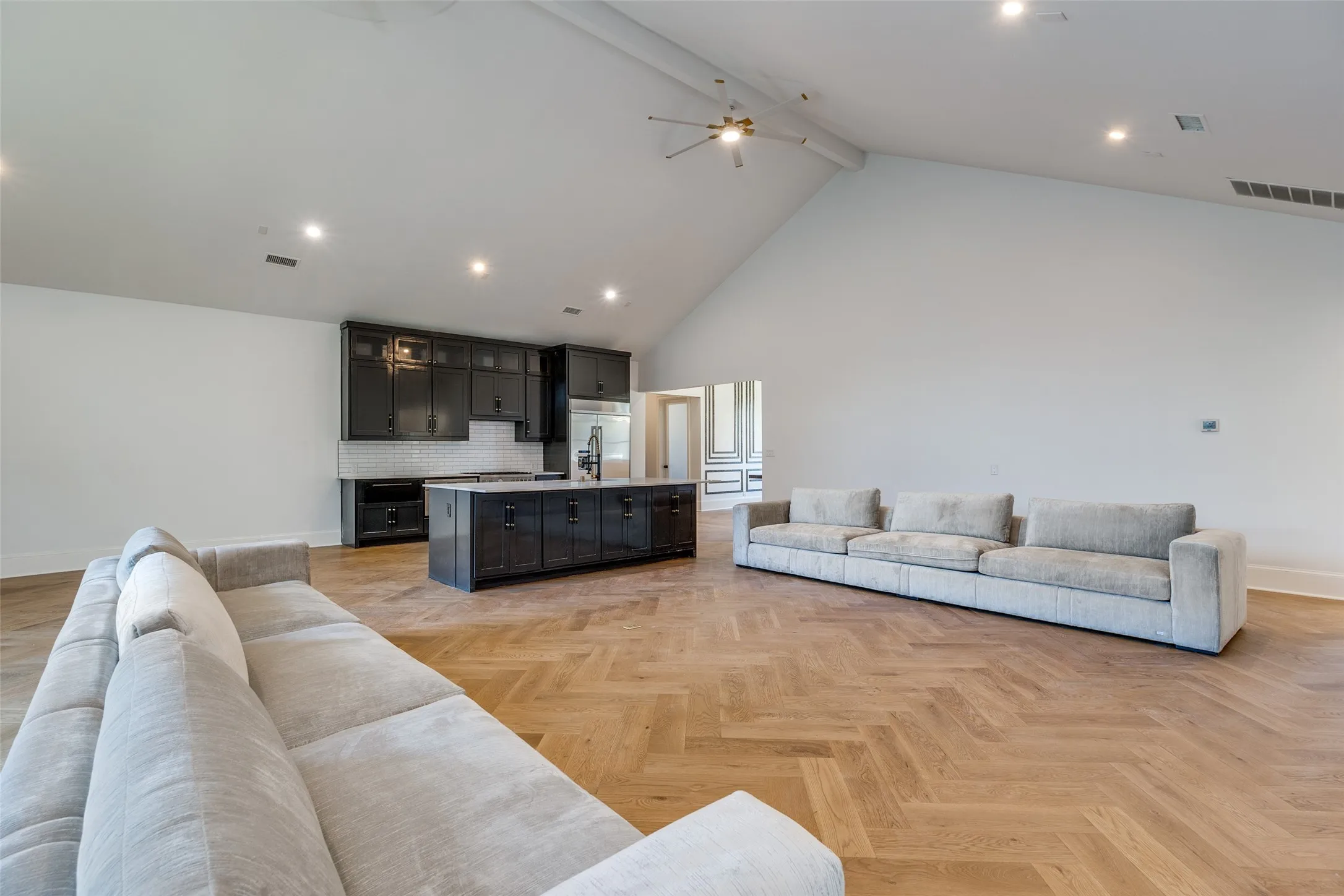 Vaulted ceiling with recessed lighting, wood-finish flooring in a herringbone pattern, dark cabinetry, kitchen island with integrated sink, and stainless steel appliances