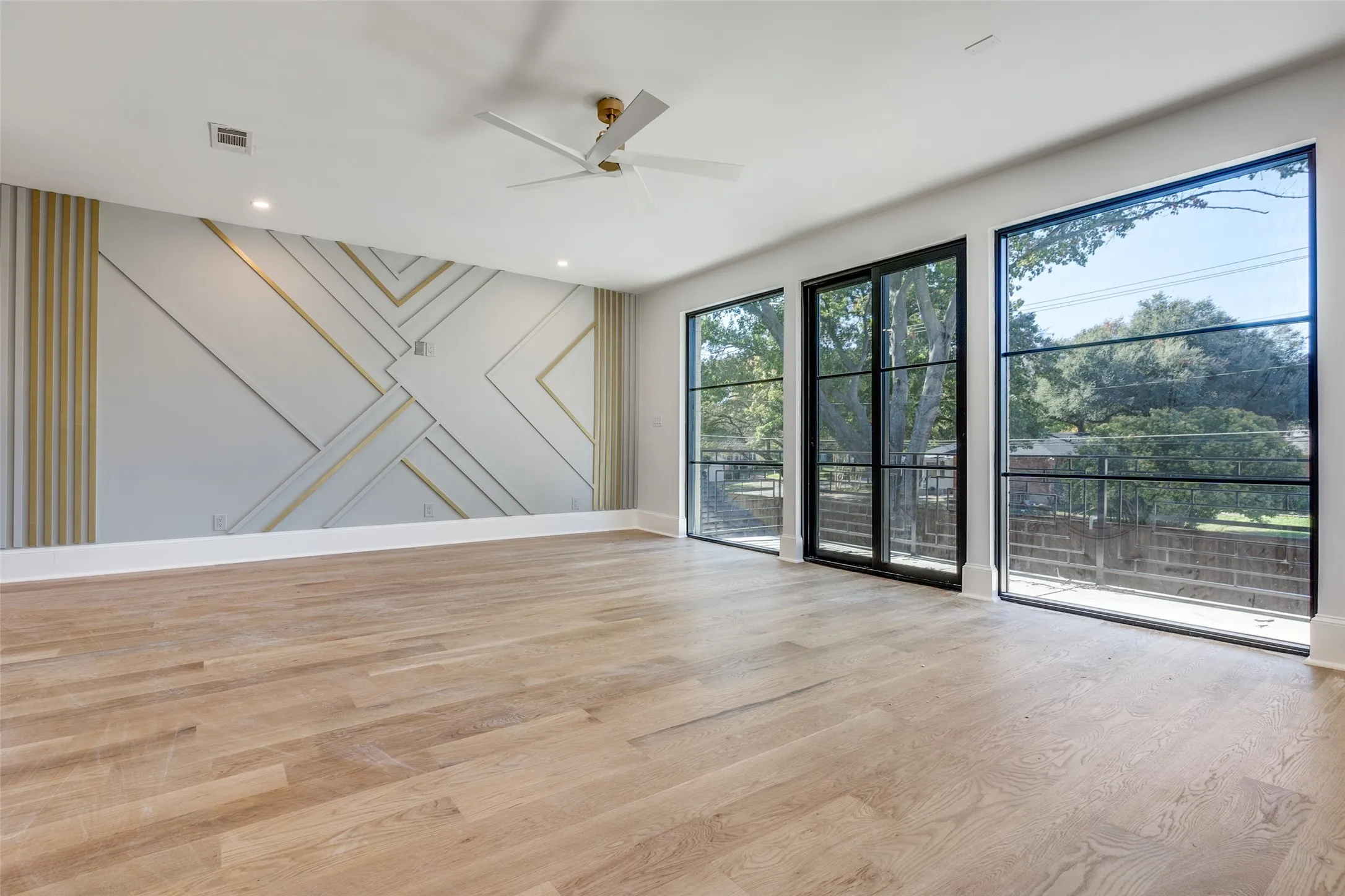 Wood-finish flooring, accent wall with geometric molding, large black-framed windows, recessed lighting, and a ceiling fan