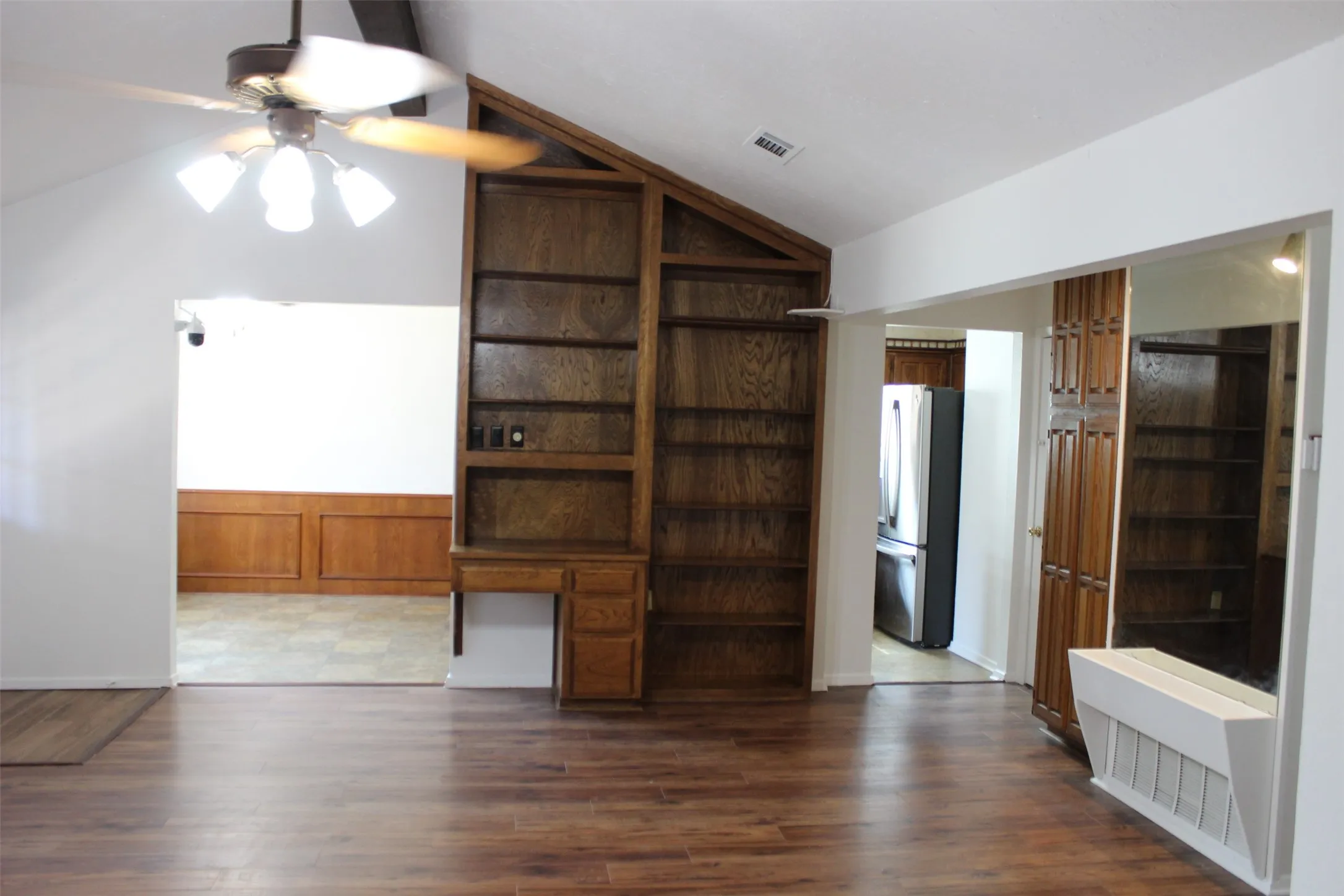 Varnished wood-finish built-in shelving with integrated desk, vaulted ceiling, wood-finish flooring, and a ceiling fan with integrated lighting