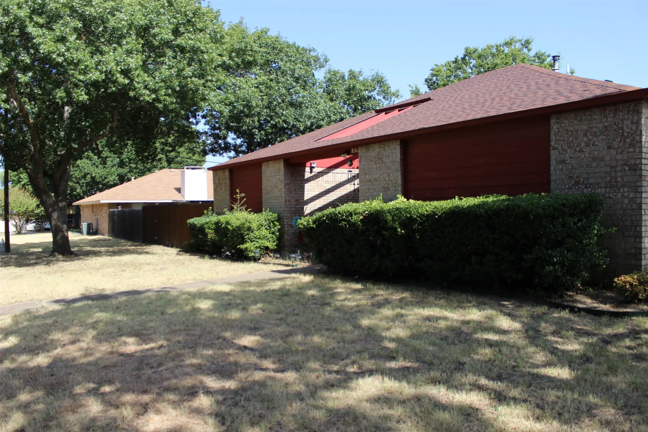 Brick exterior with horizontal siding accents, a red shingle roof, and mature perimeter hedging