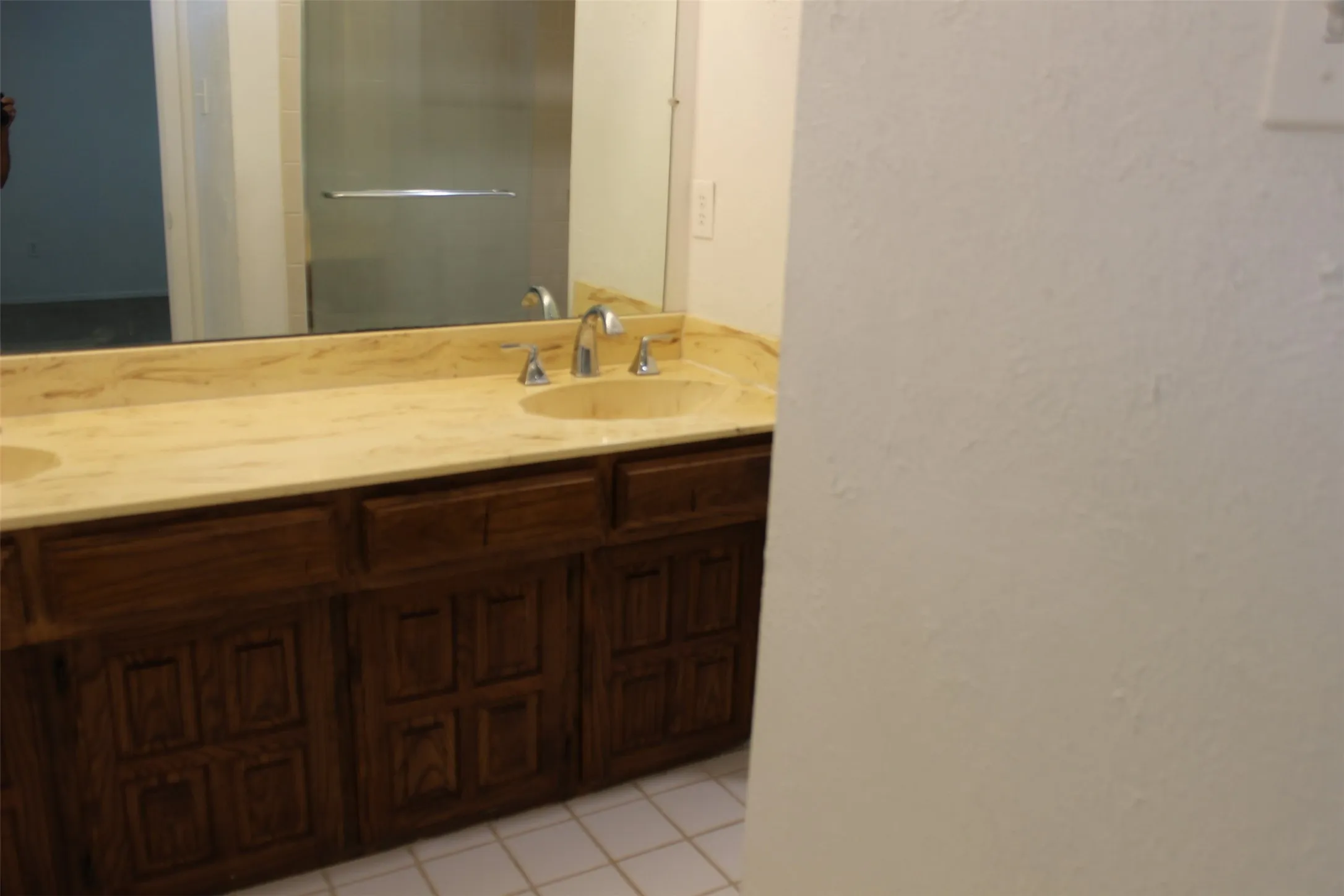 Dual vanity with integrated sinks, stone-finish countertop, and wood-finish cabinetry, set against tiled flooring
