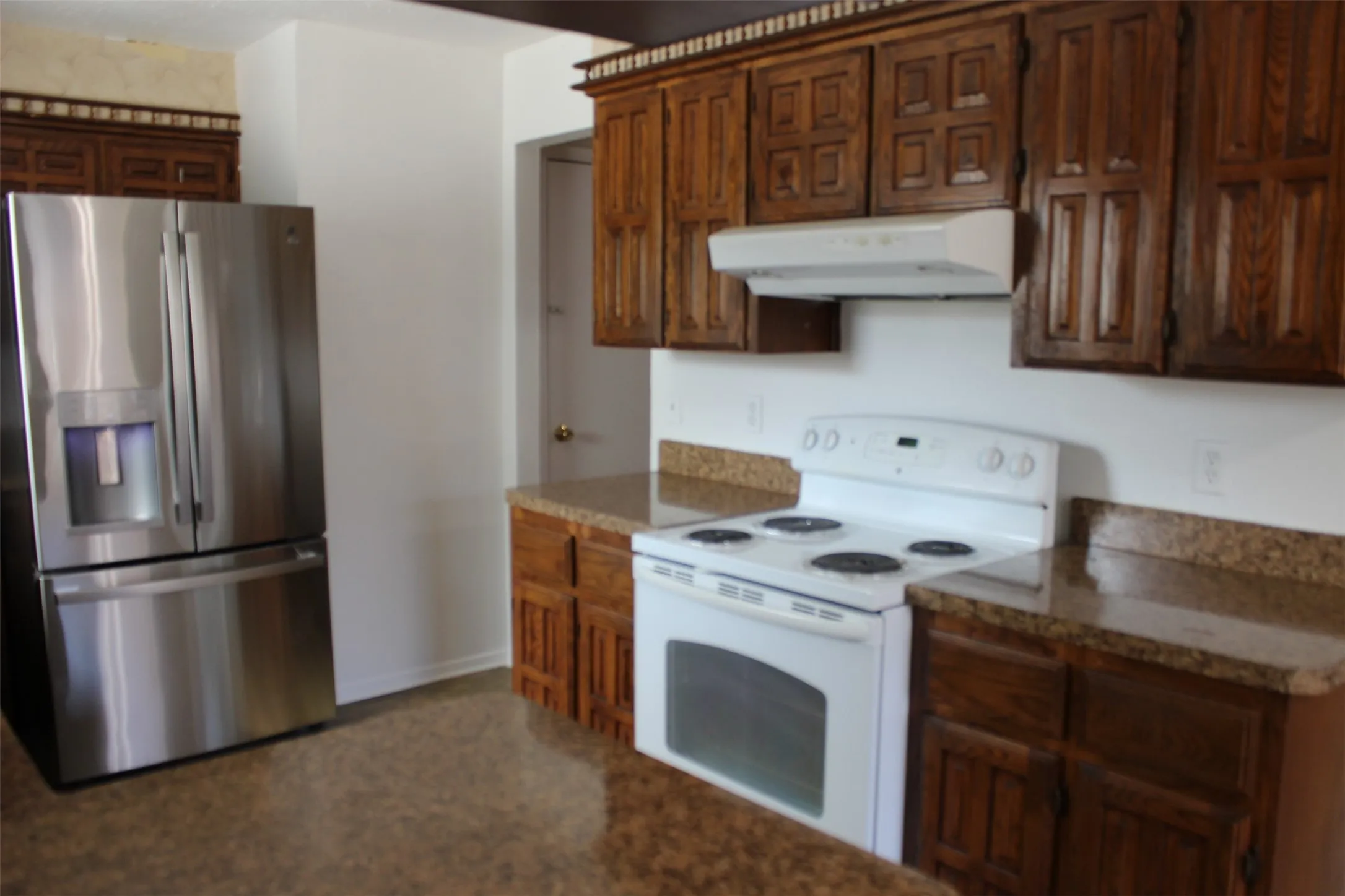 Kitchen featuring wood cabinetry, solid surface countertops, a white electric range, and a stainless steel refrigerator with an external dispenser