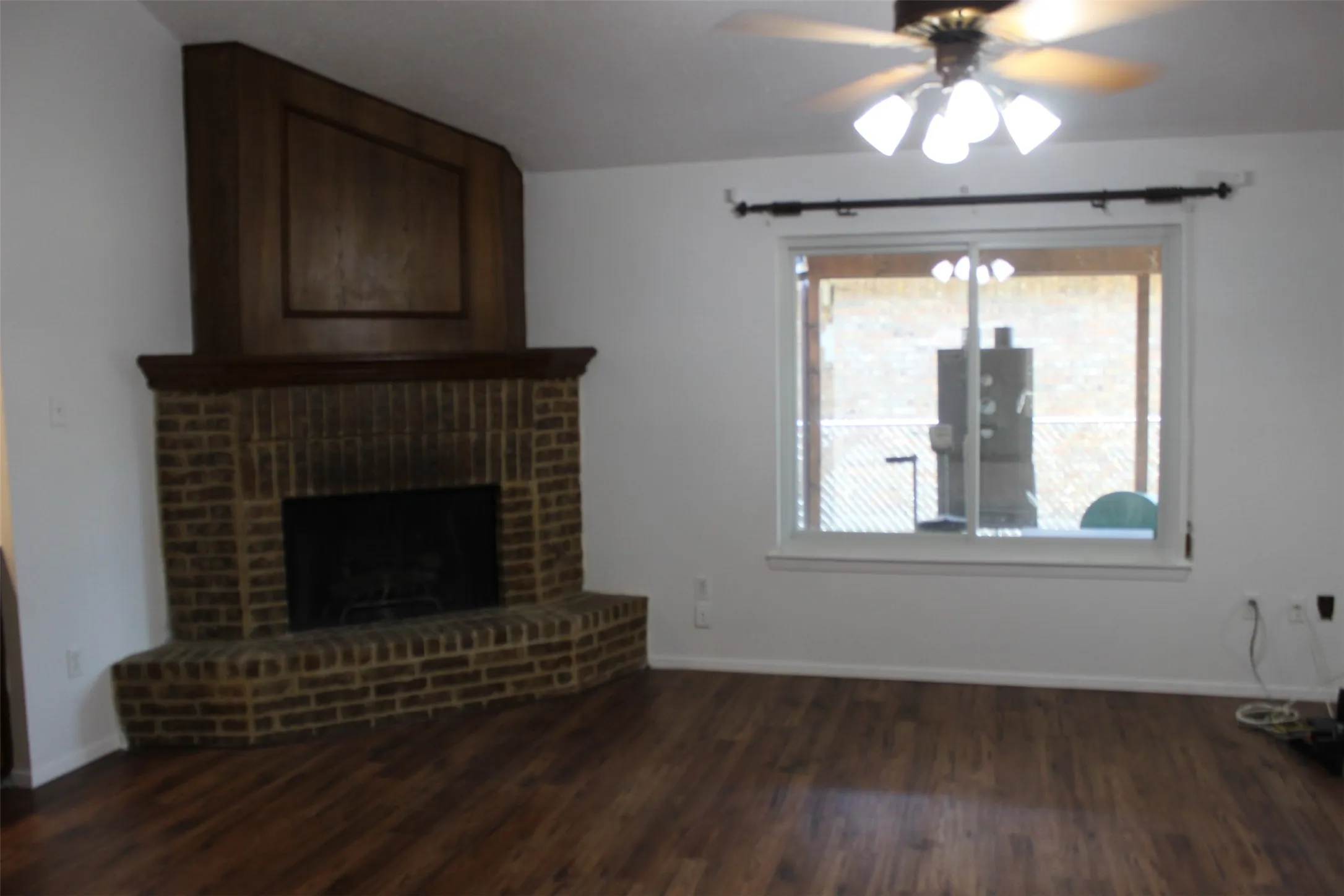 Brick fireplace with a wood-finish mantel and surround, wood-finish flooring, and a ceiling fan with integrated lighting