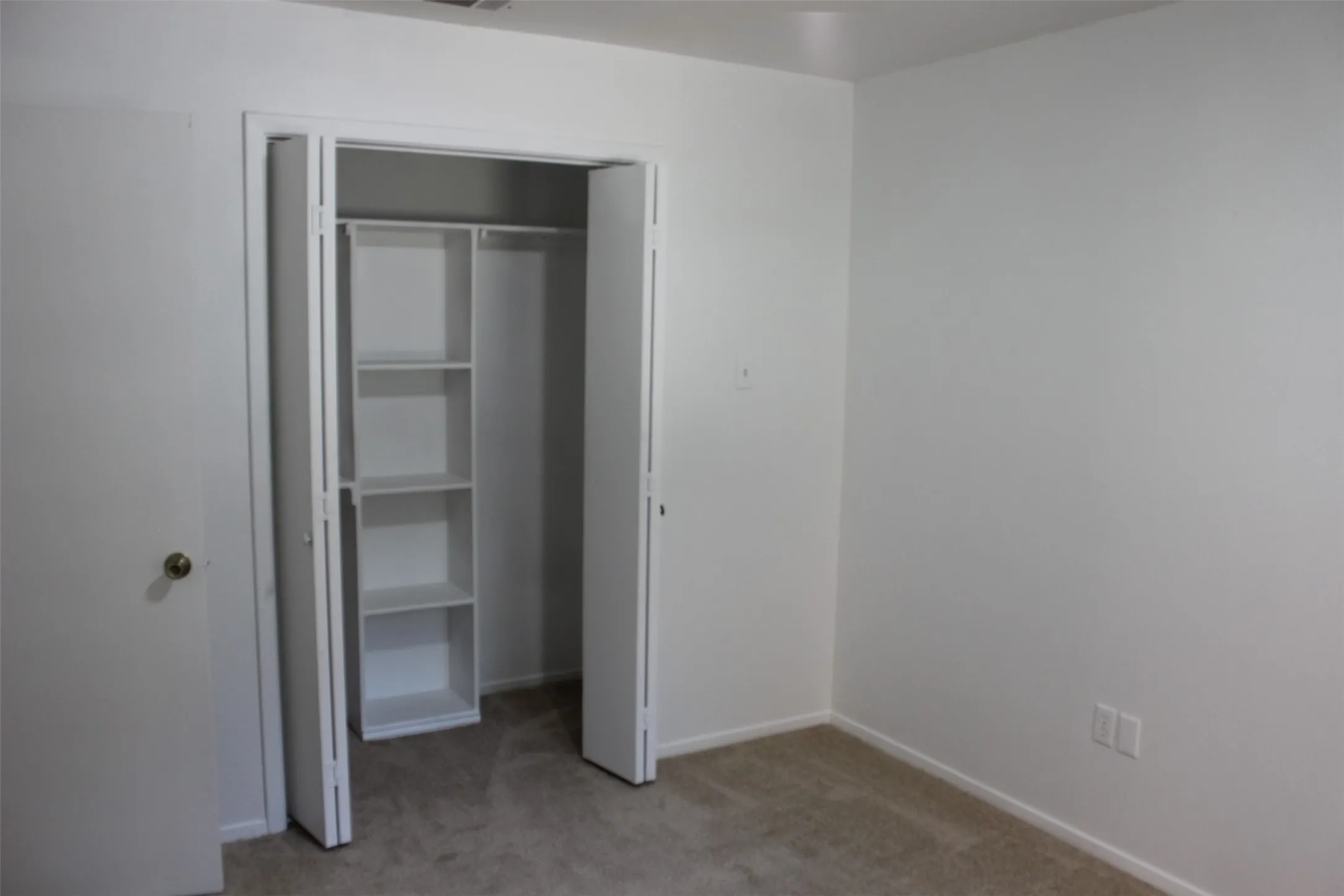 White bi-fold closet doors revealing built-in shelving and hanging rod