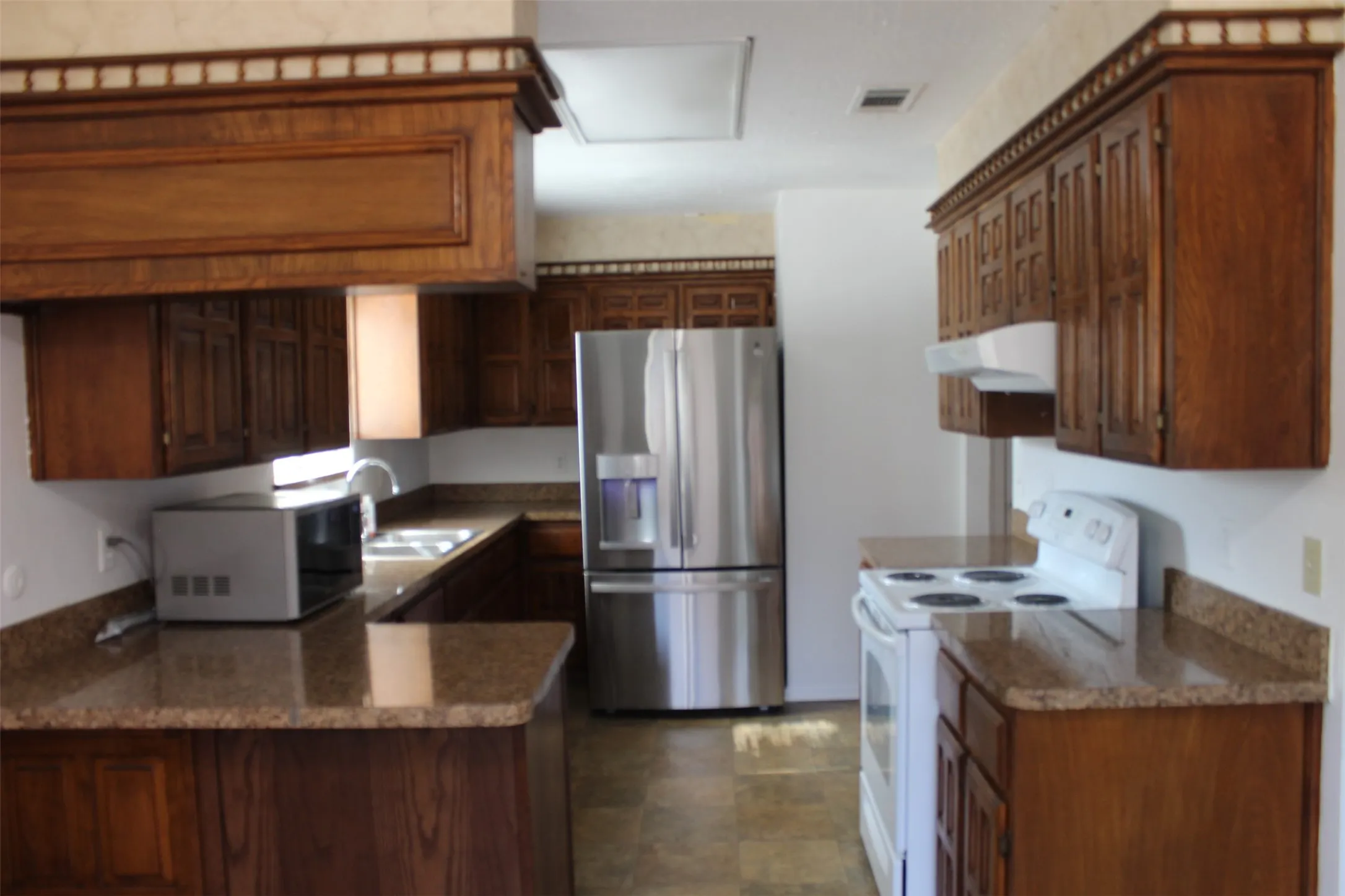 Kitchen featuring wood cabinetry, solid surface countertops, a stainless steel refrigerator, and a white electric range