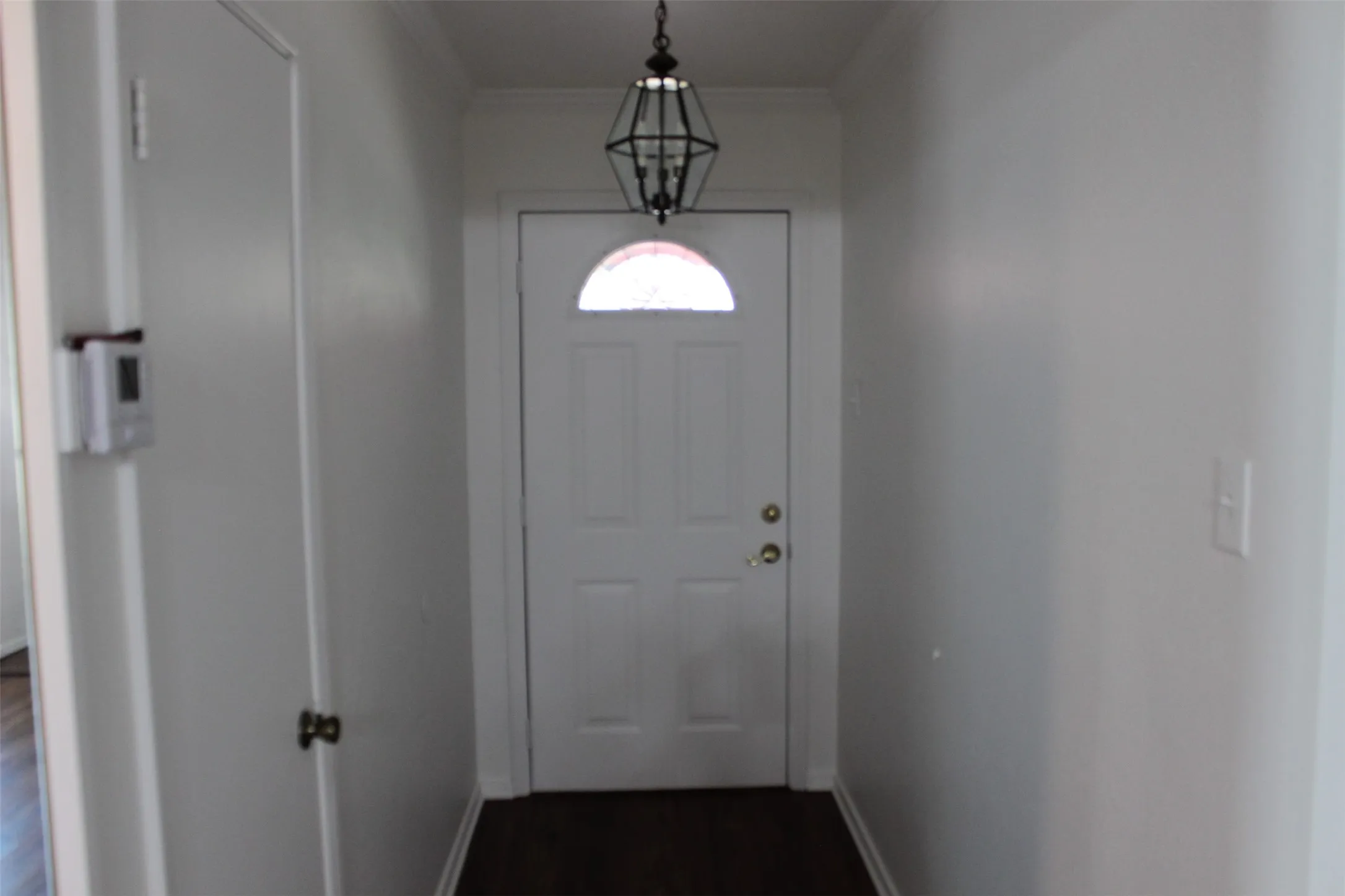 Entryway featuring a white paneled door with an arched glass insert, dark wood-finish flooring, and a decorative hanging light fixture