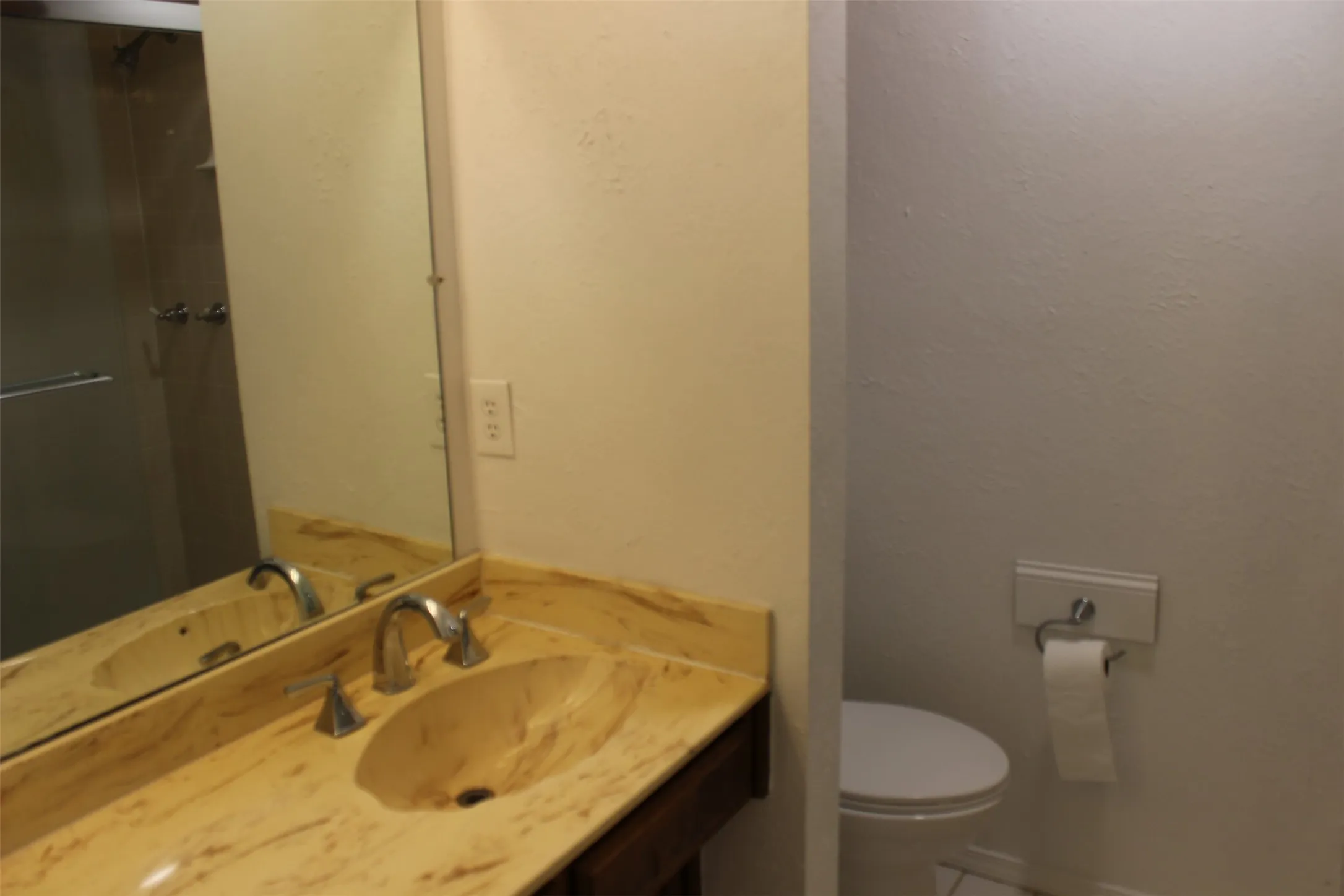 Vanity with integrated sink, chrome faucet, wall-mounted mirror, and glass-enclosed shower