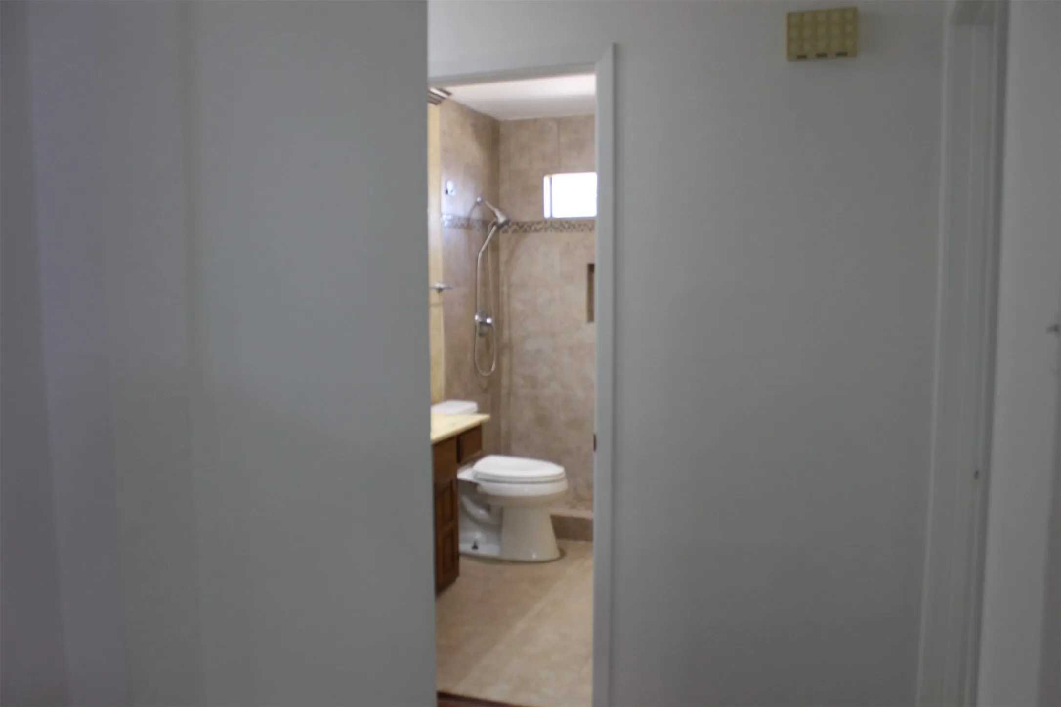 Tiled bathroom with a window, wood vanity, and a wall-mounted shower system