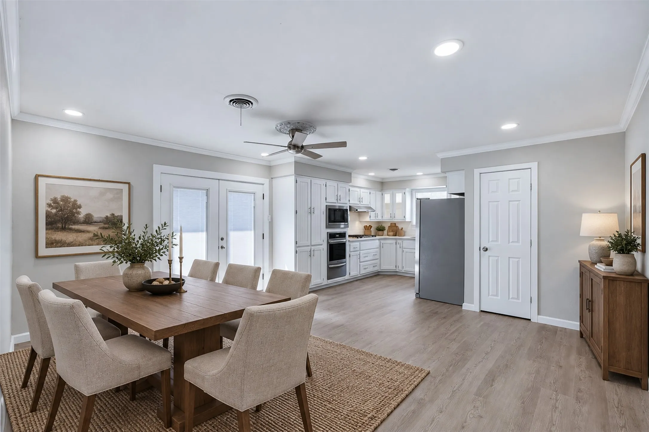 Open-concept living space with wood-finish flooring, white cabinetry, integrated stainless steel appliances, and double French doors