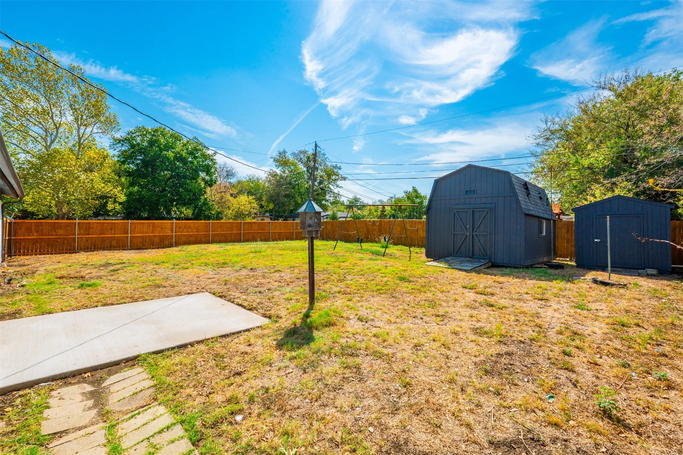 Expansive backyard featuring a new wood privacy fence, concrete patio area, and two detached storage sheds