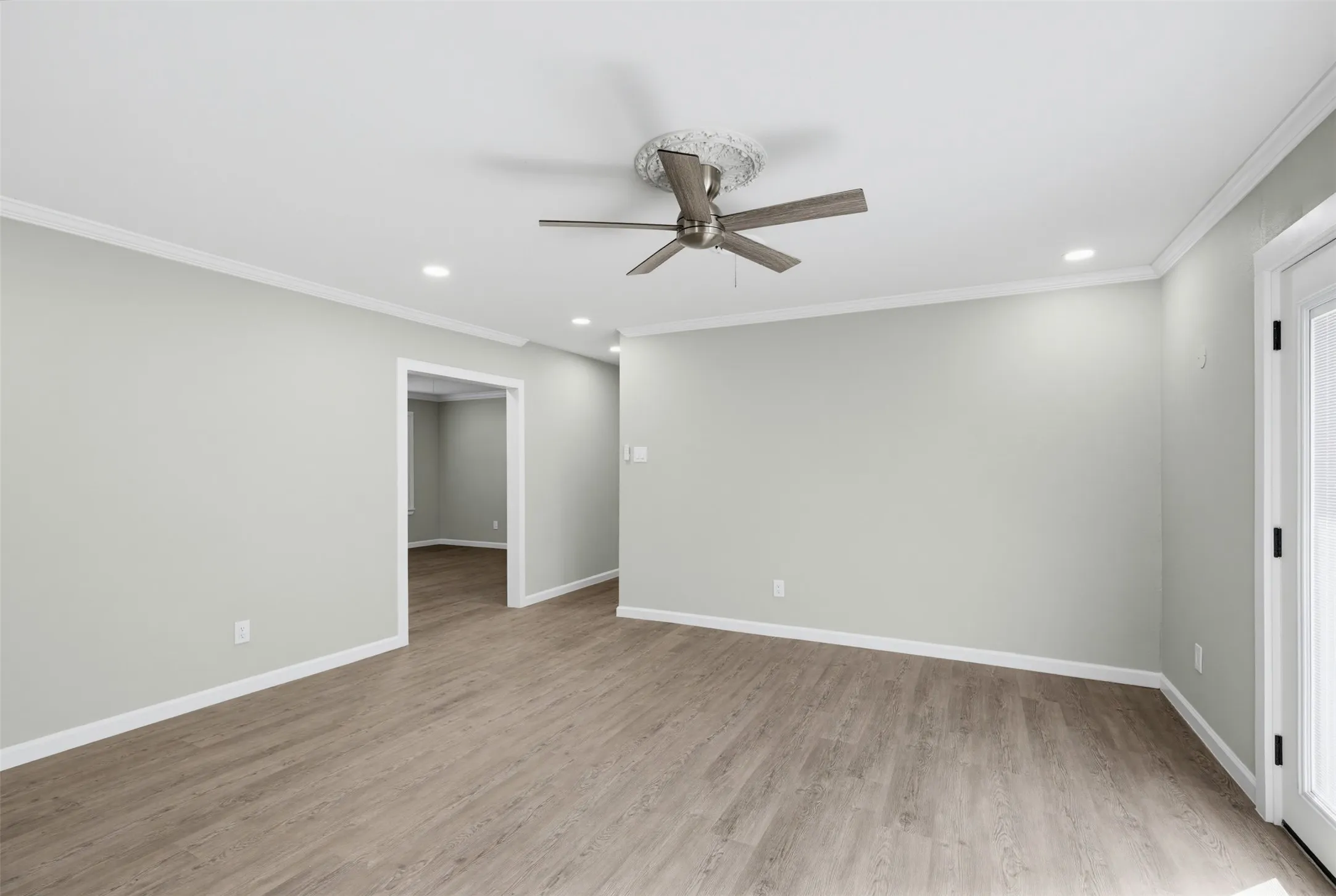 Wood-finish flooring, recessed lighting, crown molding, ceiling fan, and white trim throughout