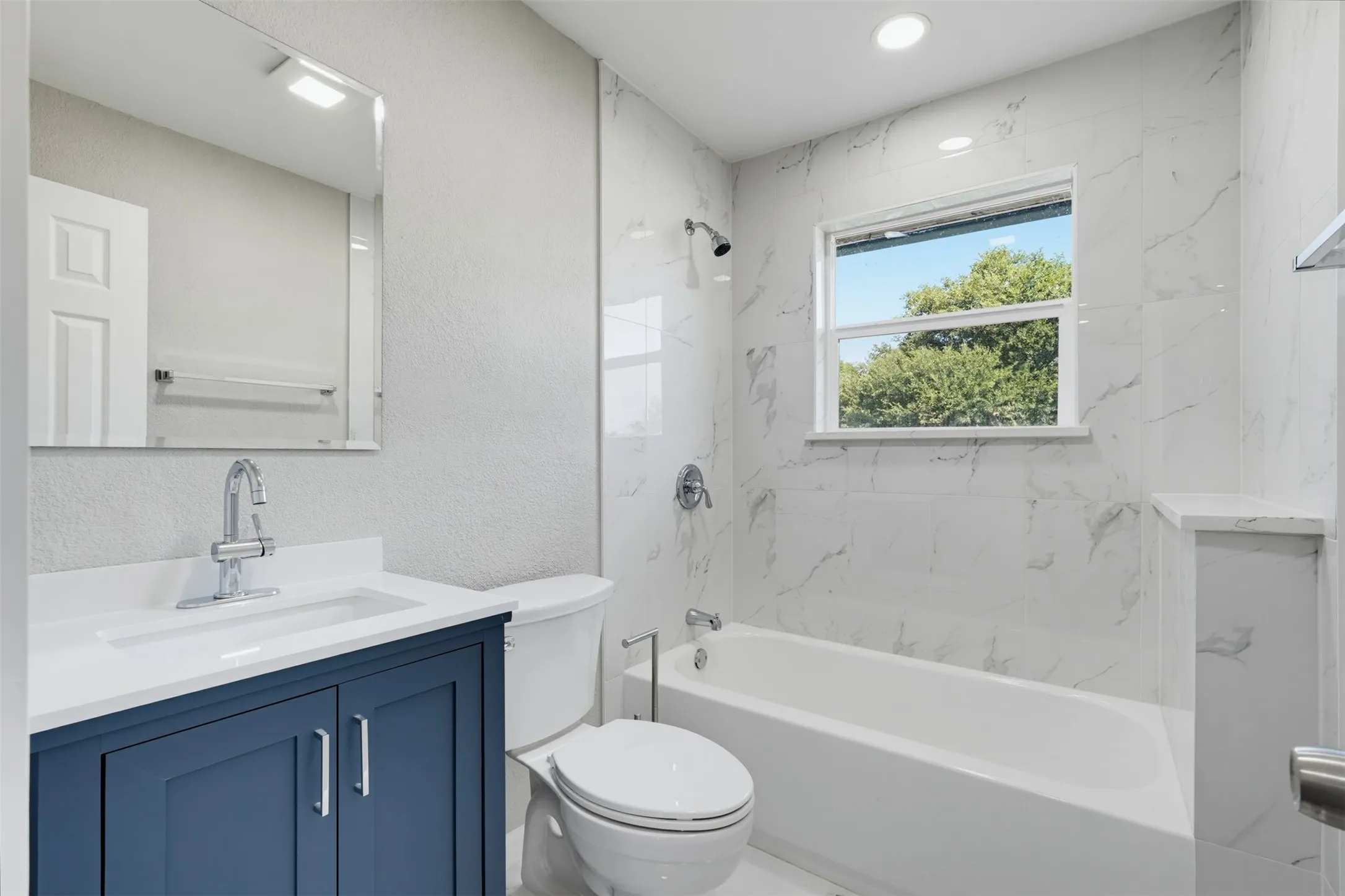 White tiled shower surround with built-in niche, white bathtub, and recessed lighting