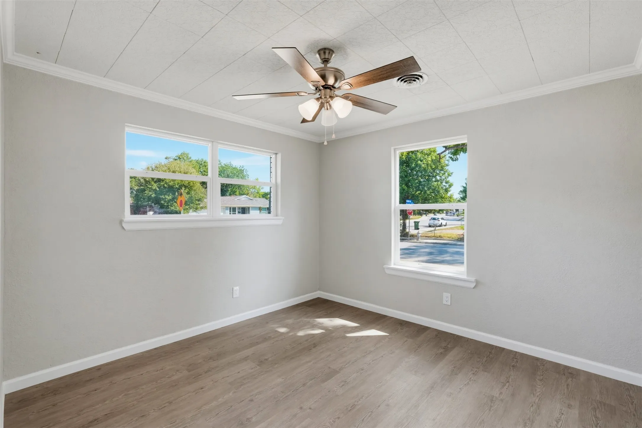 Room featuring two windows, wood-finish flooring, a ceiling fan with integrated lighting, and crown molding