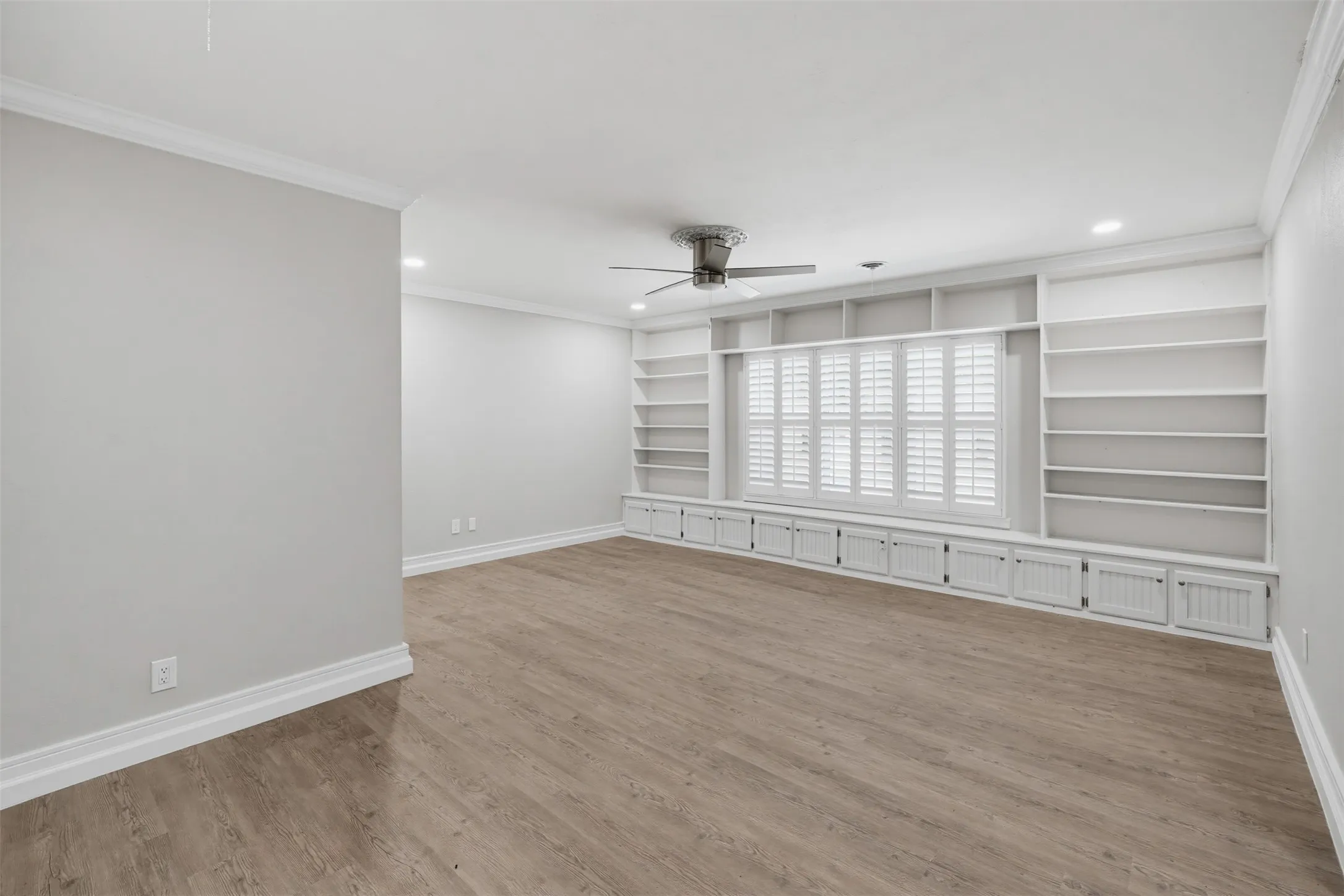 Wood-finish flooring, crown molding, a ceiling fan, recessed lighting, and built-in shelving with lower cabinetry