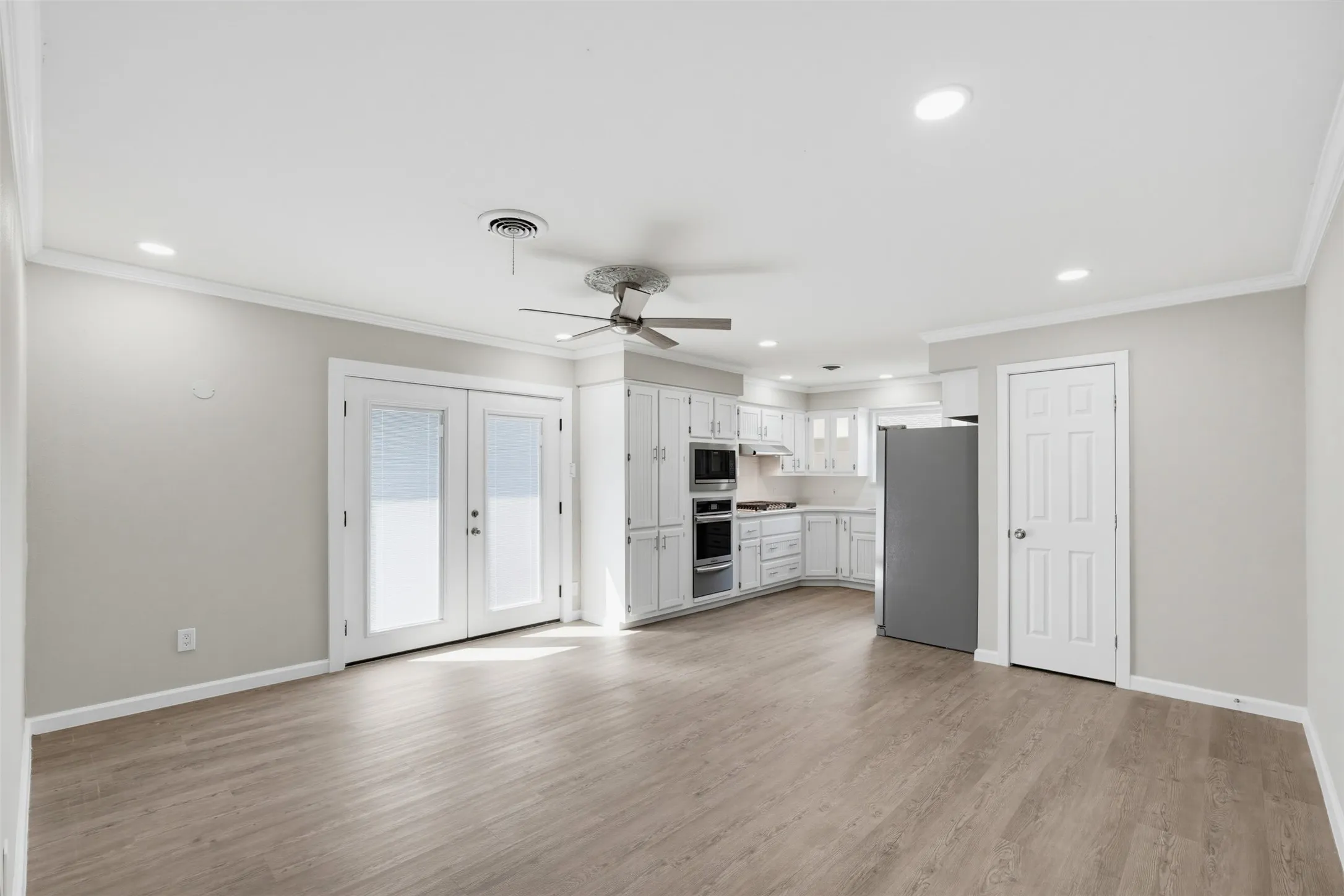 Open-concept living area featuring wood-finish flooring, recessed lighting, a ceiling fan, and white French doors