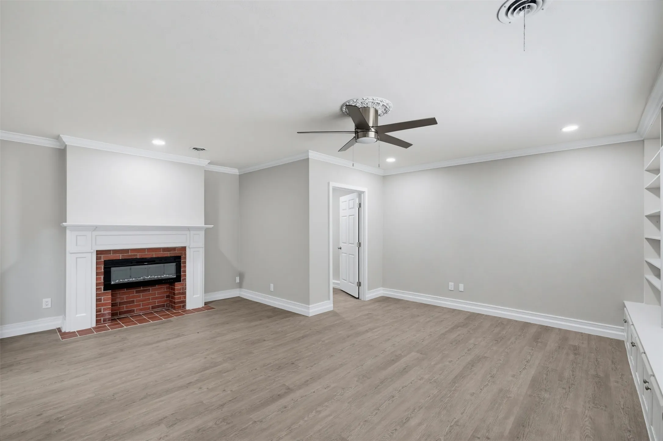 Wood-finish flooring, white crown molding, brick fireplace with mantel, recessed lighting, and ceiling fan