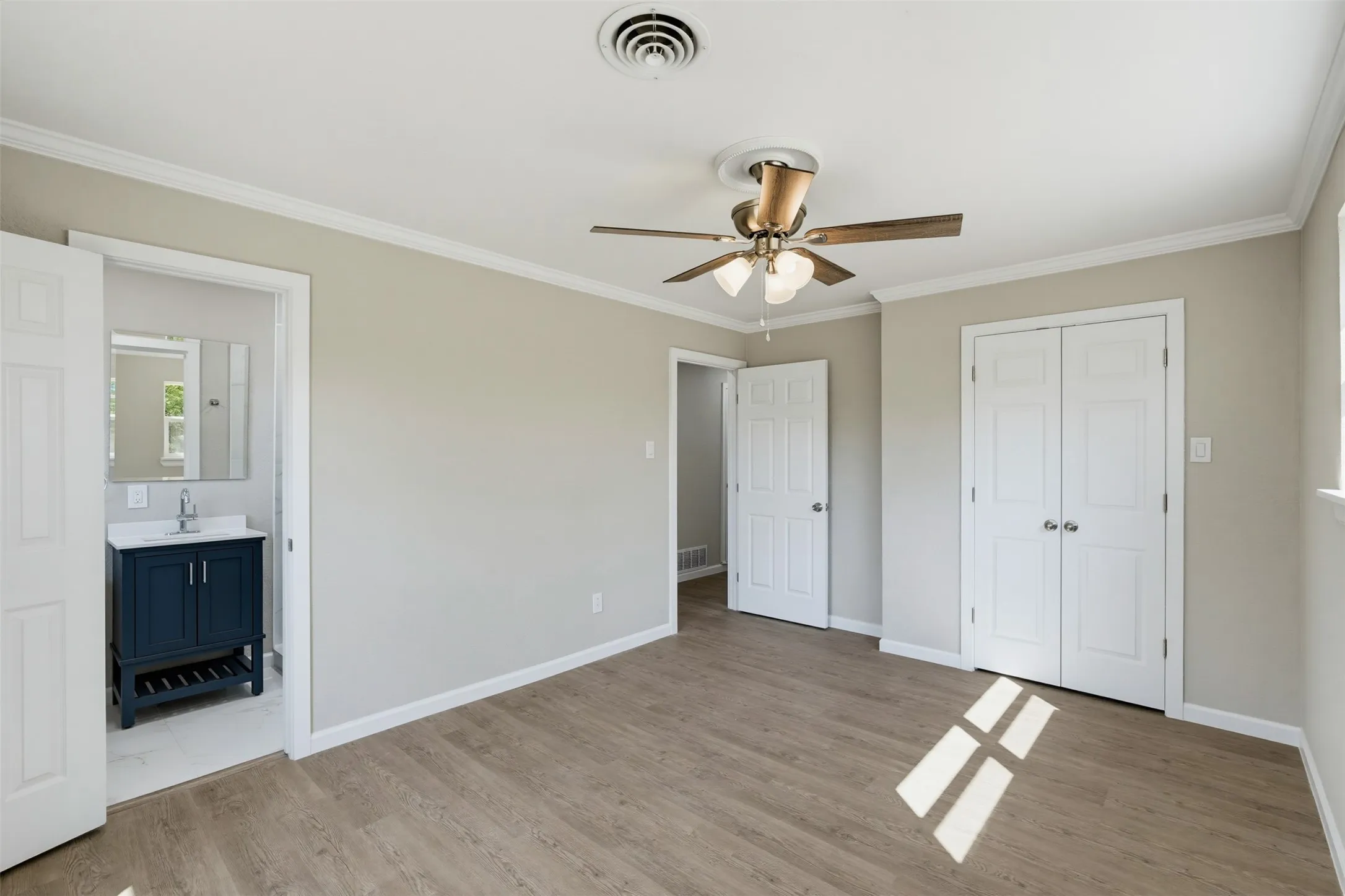Wood-finish flooring, ceiling fan with integrated lighting, white crown molding, white painted trim, and a built-in closet with bi-fold doors