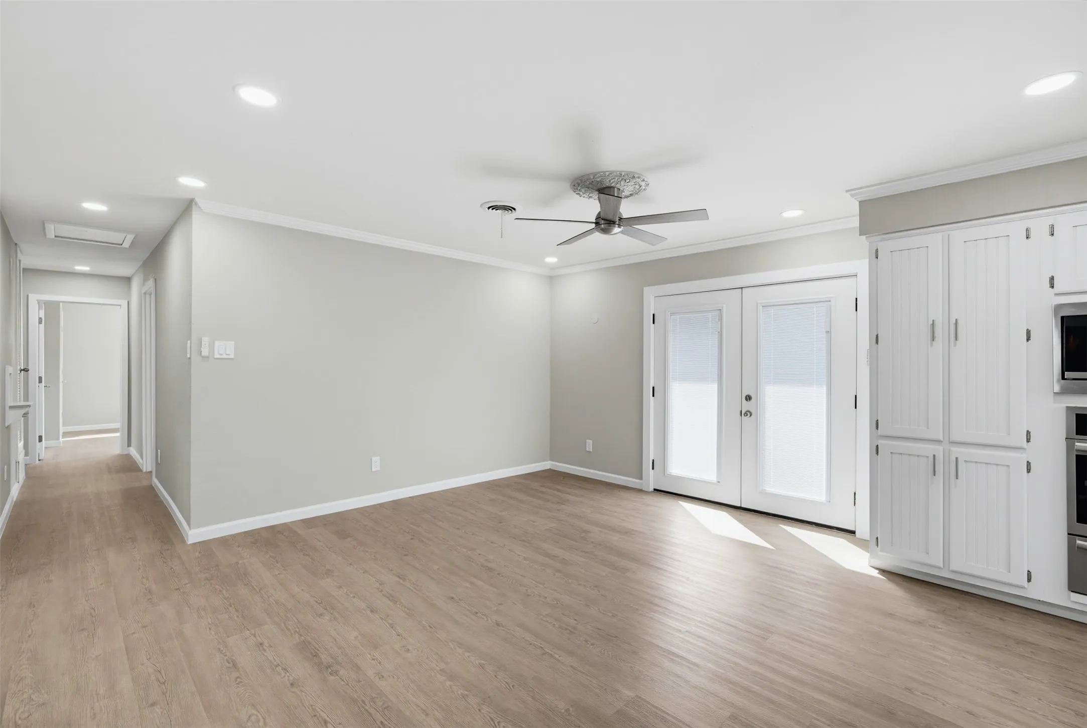 Recessed ceiling lighting, wood-finish flooring, ceiling fan, white paneled cabinetry, and double French doors