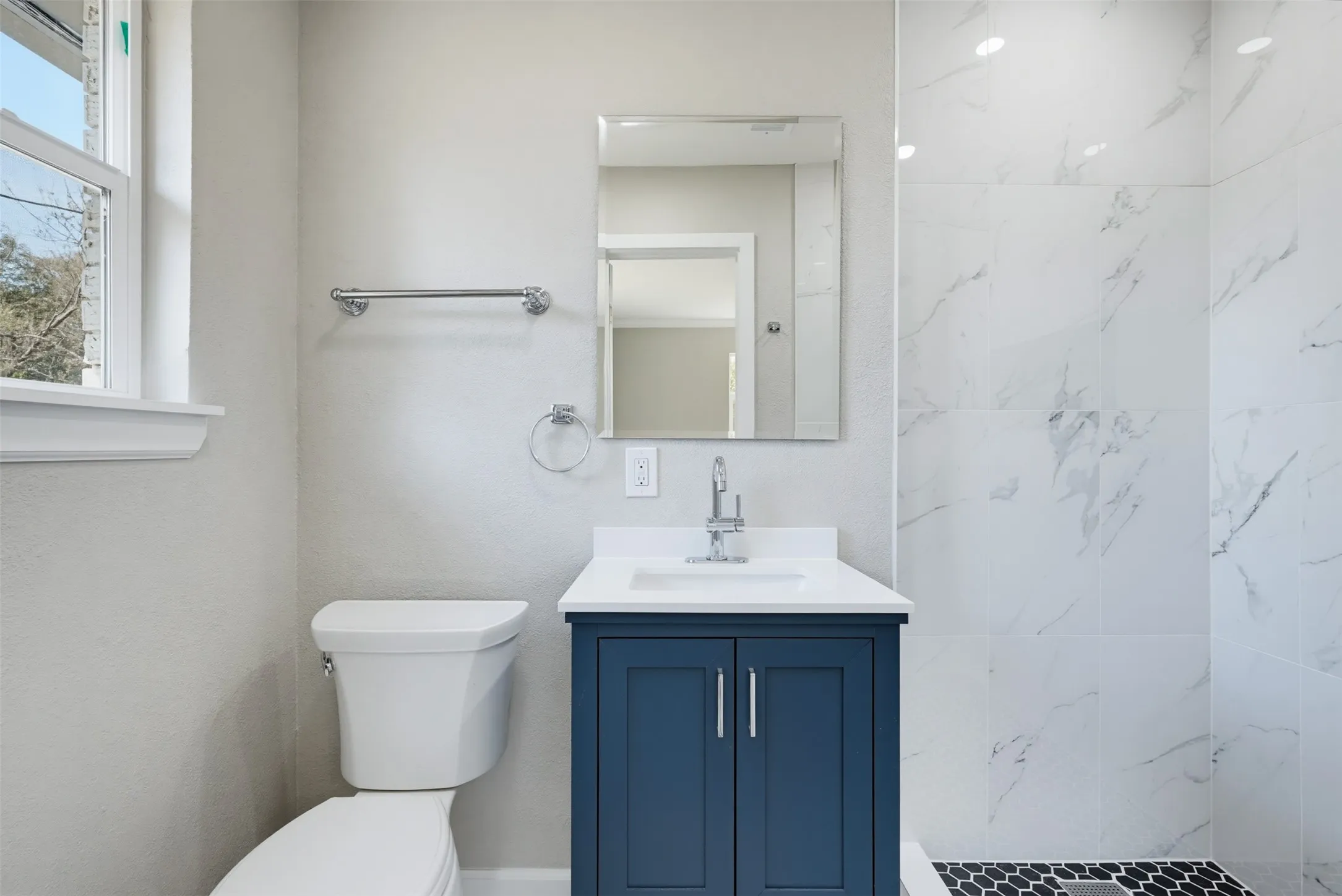 Bathroom featuring a blue vanity with a white countertop, a white toilet, white wall tiling, and black hexagonal floor tiling in the shower