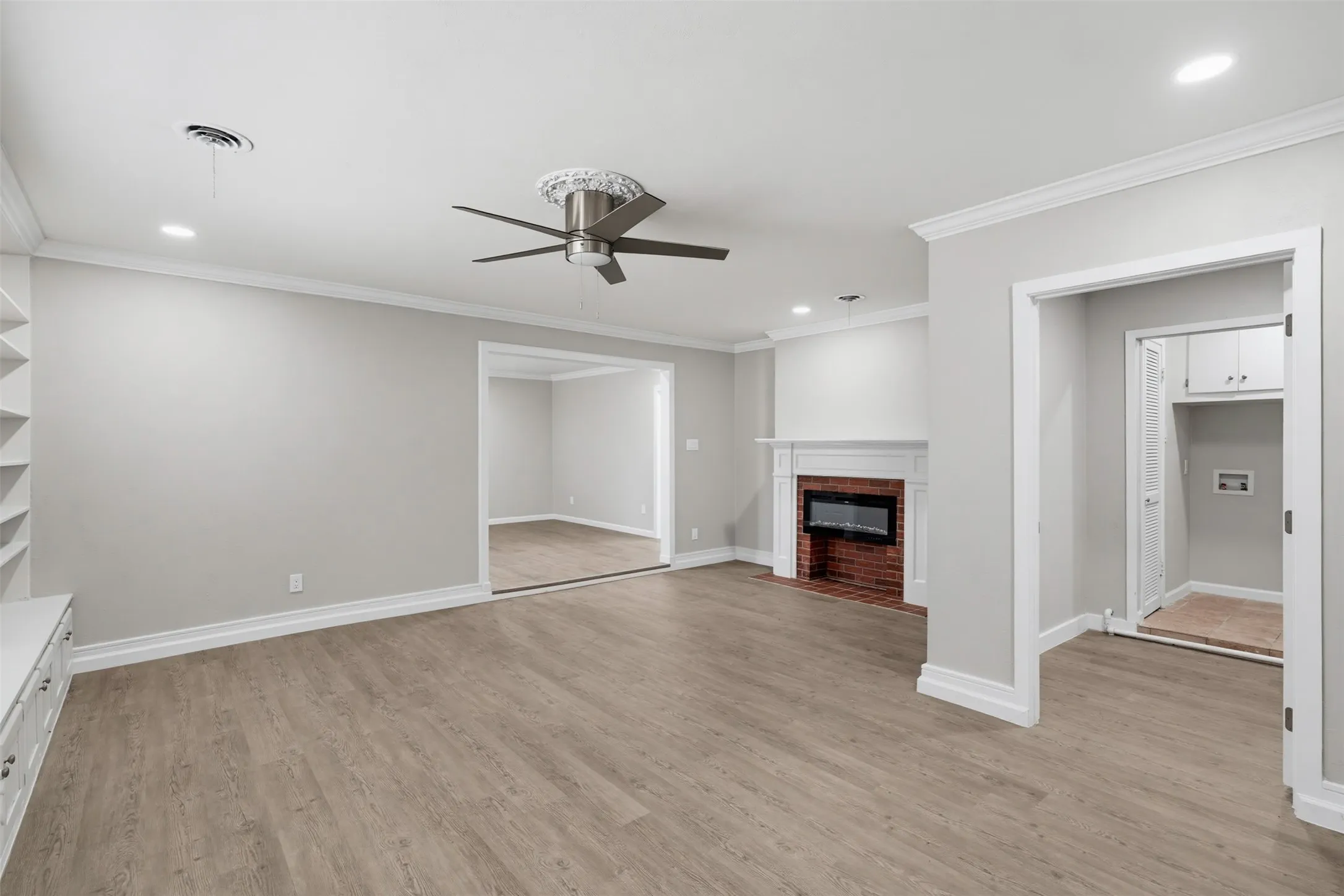 Spacious interior featuring wood-finish flooring, a brick fireplace with mantel, ceiling fan, recessed lighting, and built-in shelving