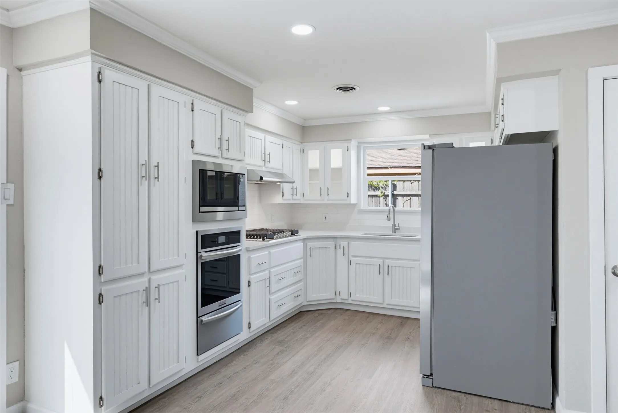 White cabinetry with beadboard accents, stainless steel appliances, recessed lighting, wood-finish flooring, and a countertop-mounted sink