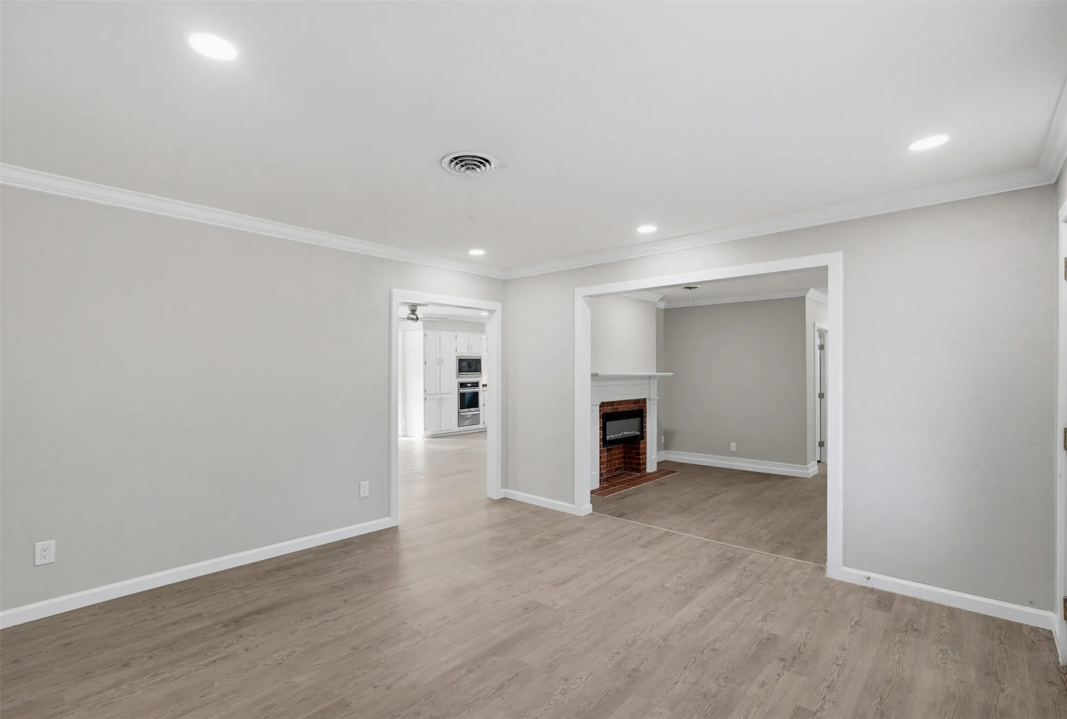 Recessed lighting, crown molding, wood-finish flooring, brick fireplace with white mantel, white cabinetry