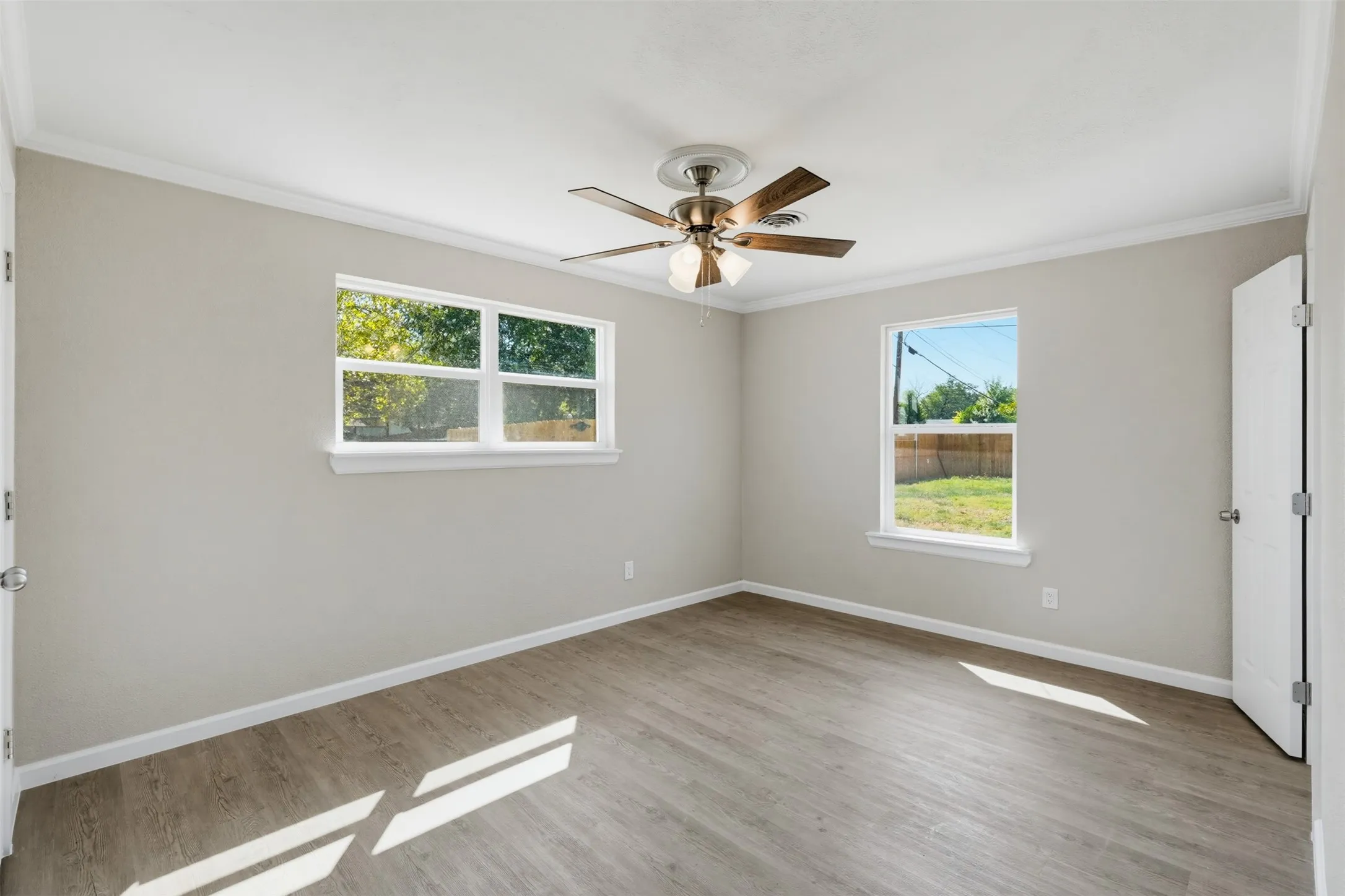 Wood-finish flooring with crown molding and a ceiling fan